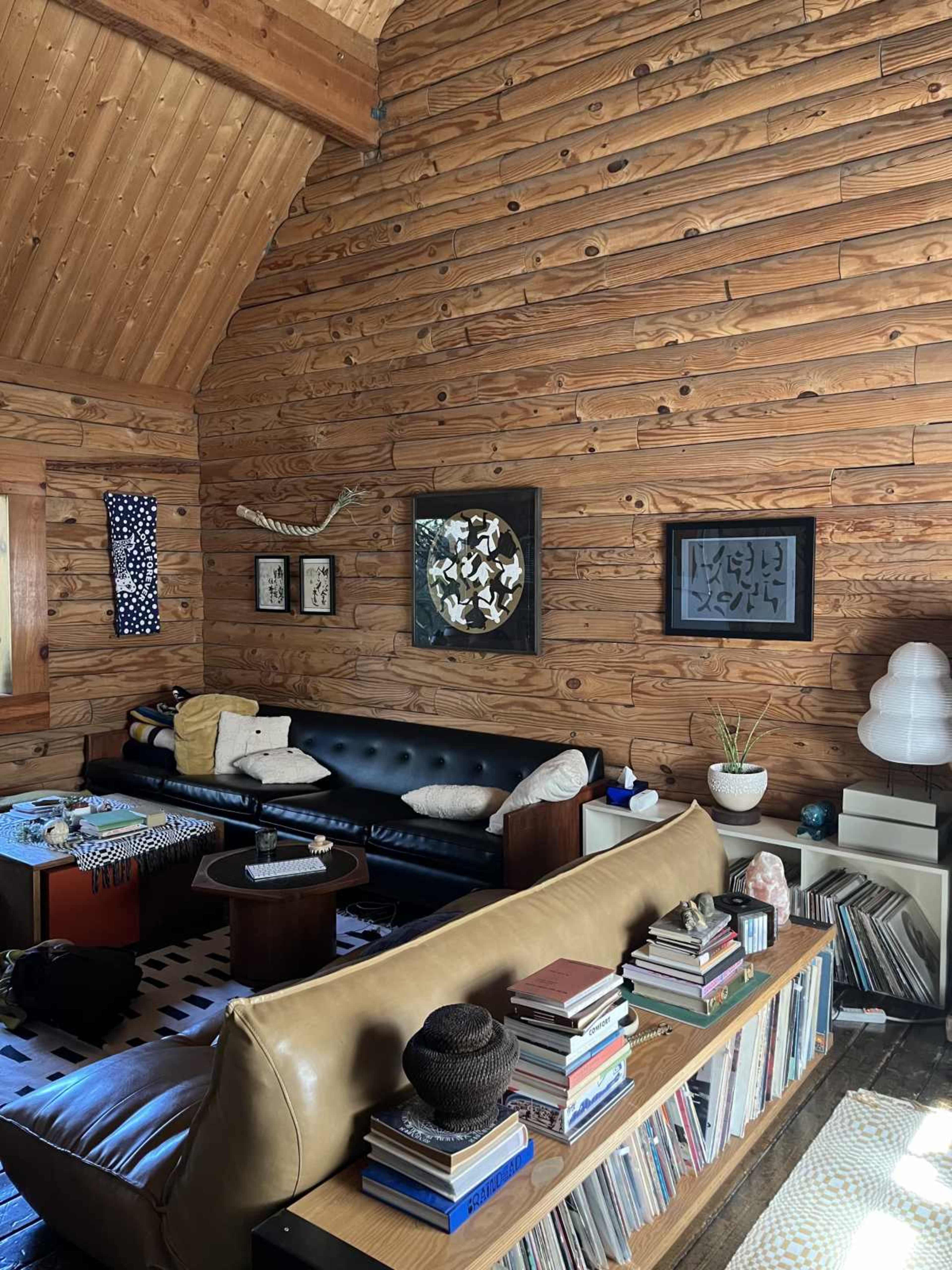 The image shows a wooden-paneled living room with a black sofa, a coffee table, and shelves of books and decorative items.