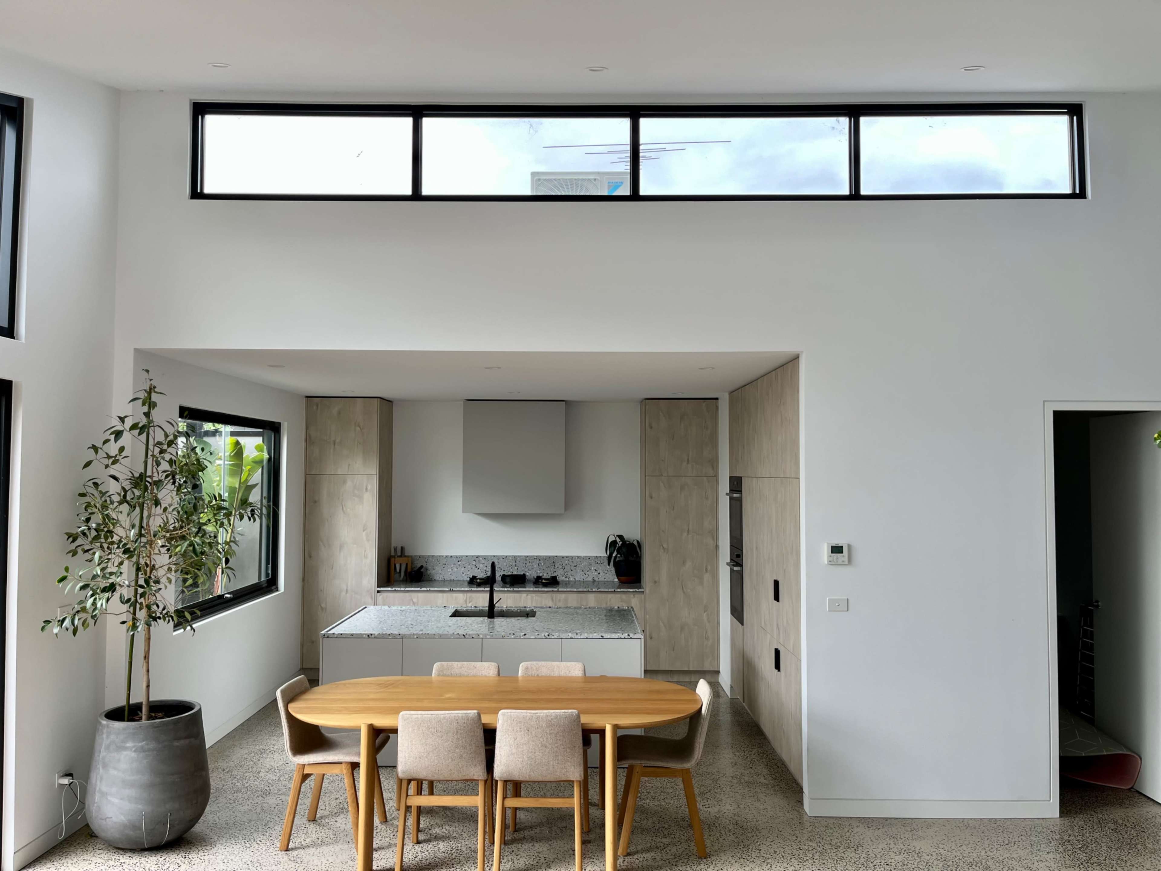 A modern kitchen and dining area features a sleek table with four chairs, large windows, and minimalist cabinetry.