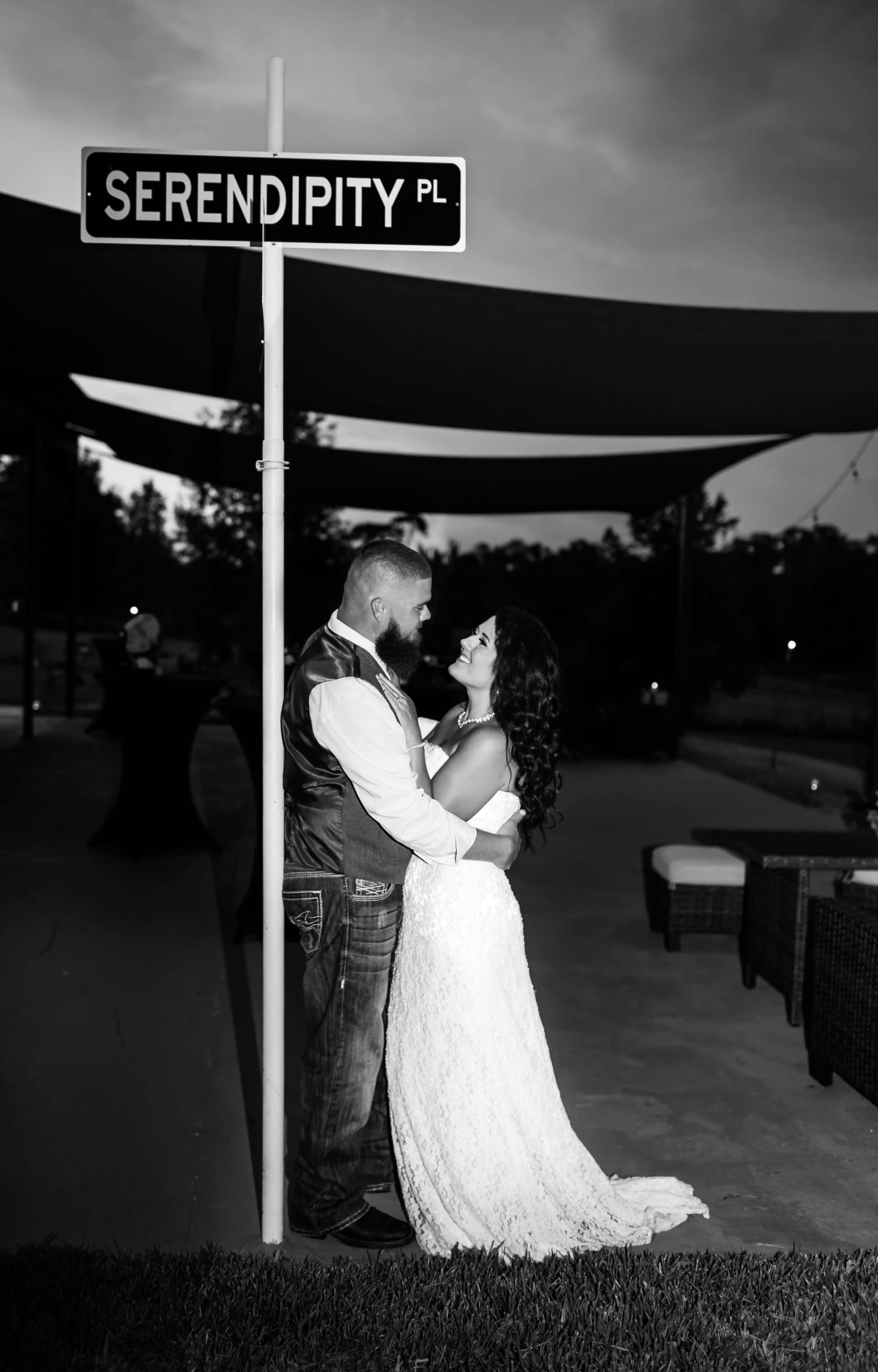 A couple embraces near a street sign labeled "SERENDIPITY PL" under a shaded area with outdoor seating.