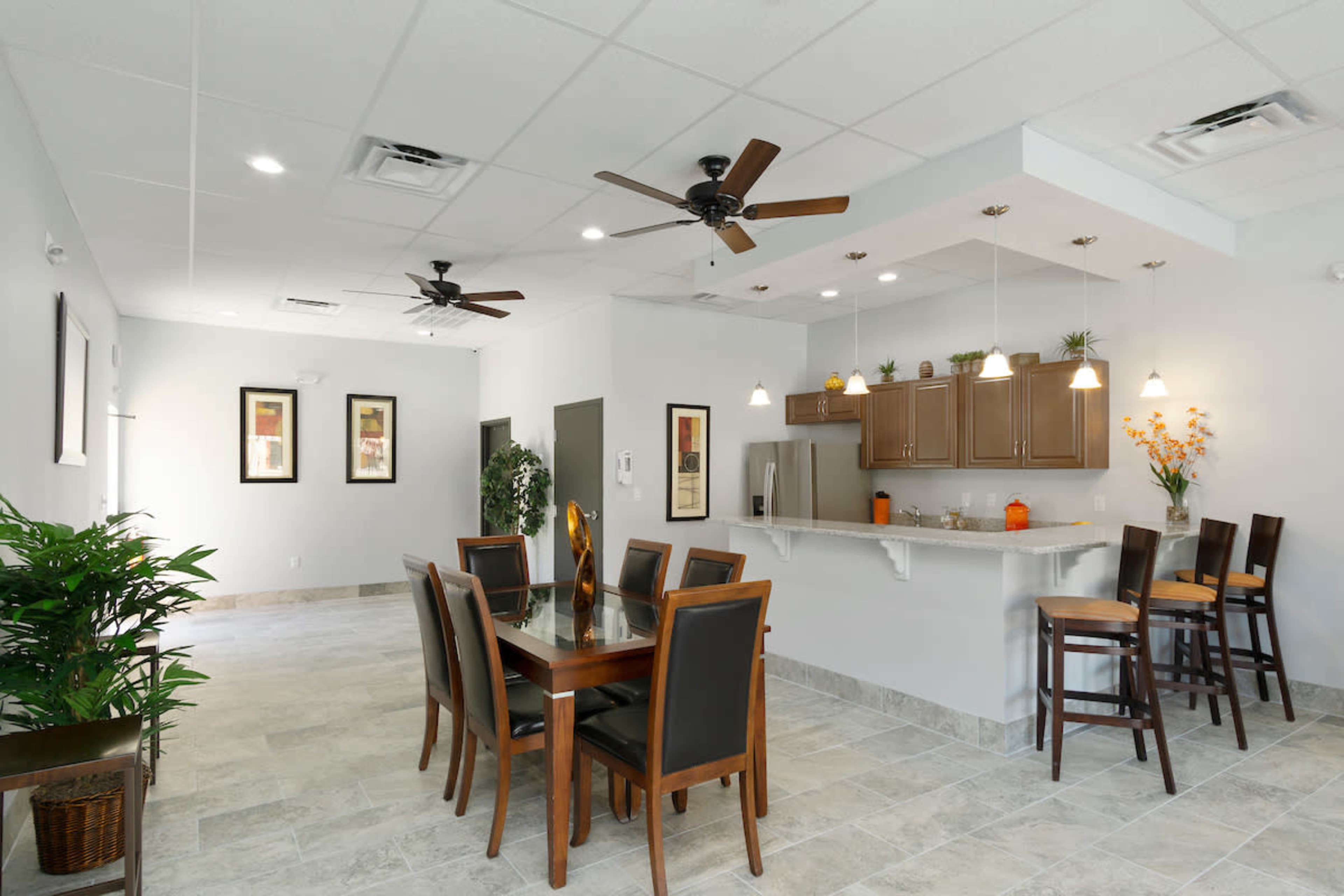 A modern dining area with a wooden table and chairs, a breakfast bar, and kitchen cabinetry, all under ceiling fans and bright lighting.