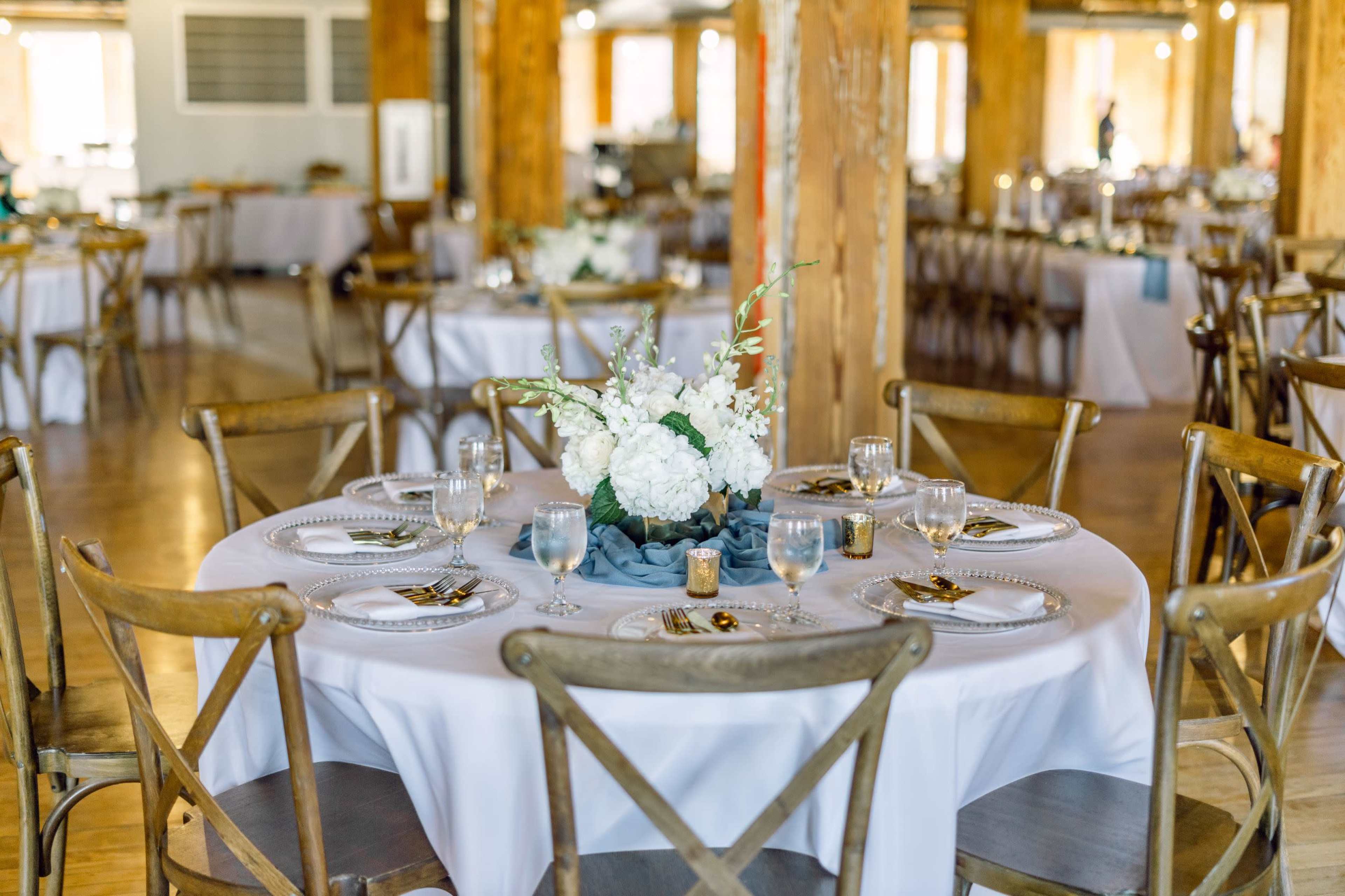 A round dining table elegantly set with plates, glasses, and a floral centerpiece in a large event space.