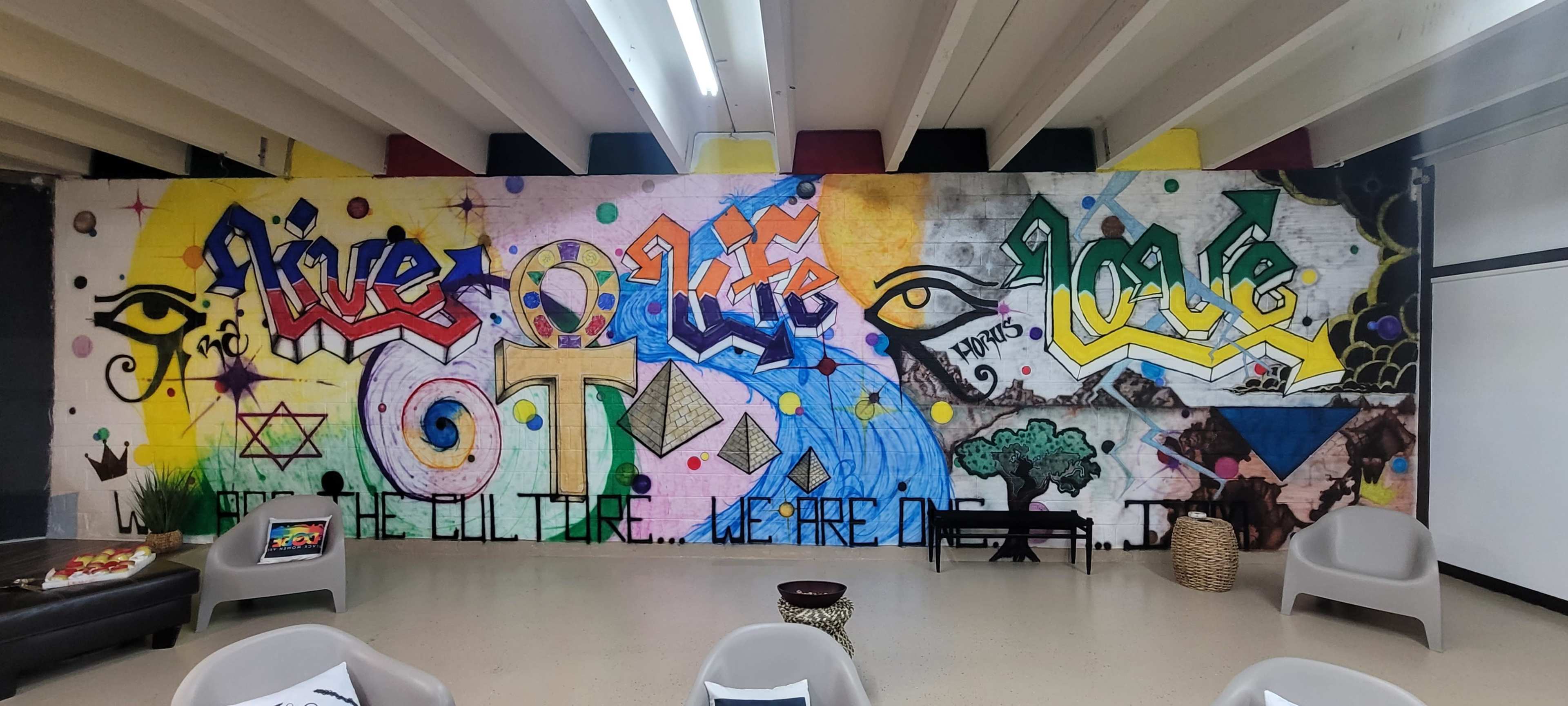 A mural on a wall featuring vibrant graffiti with the words "Rise," "Life," and "Love," along with various symbols and colorful patterns.