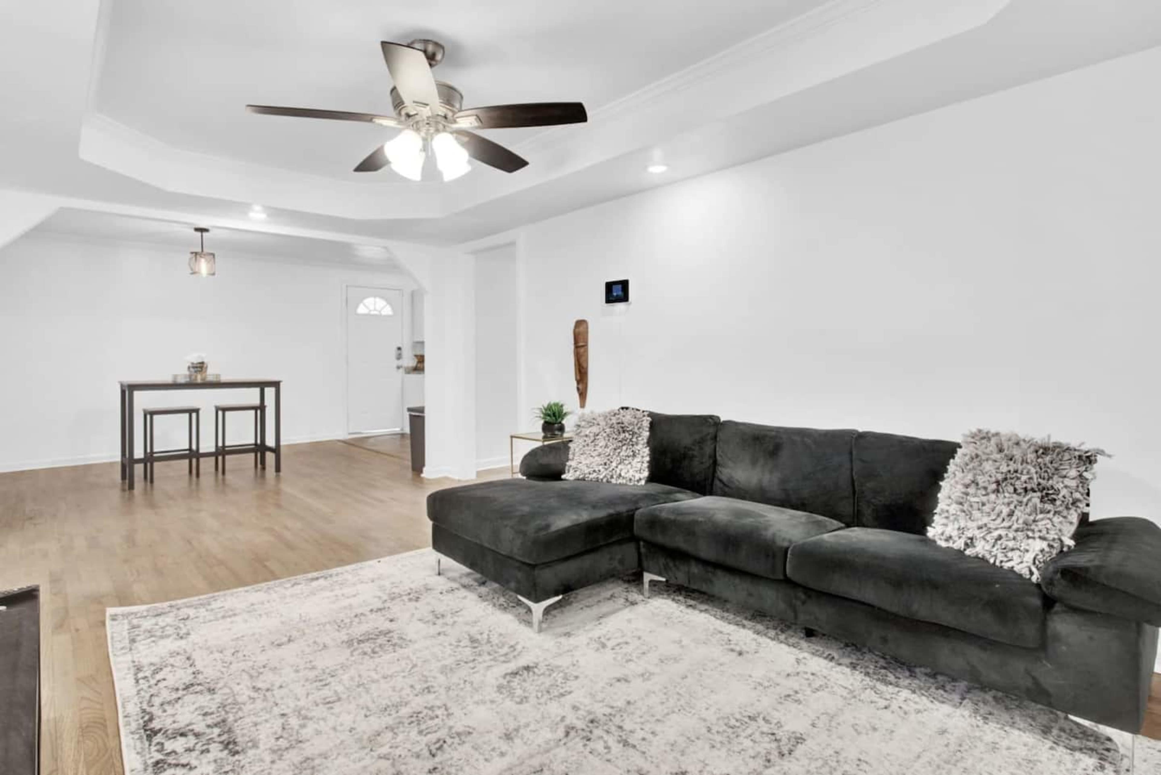 A living area with a dark sofa, a large area rug, and a table with two stools in the background.