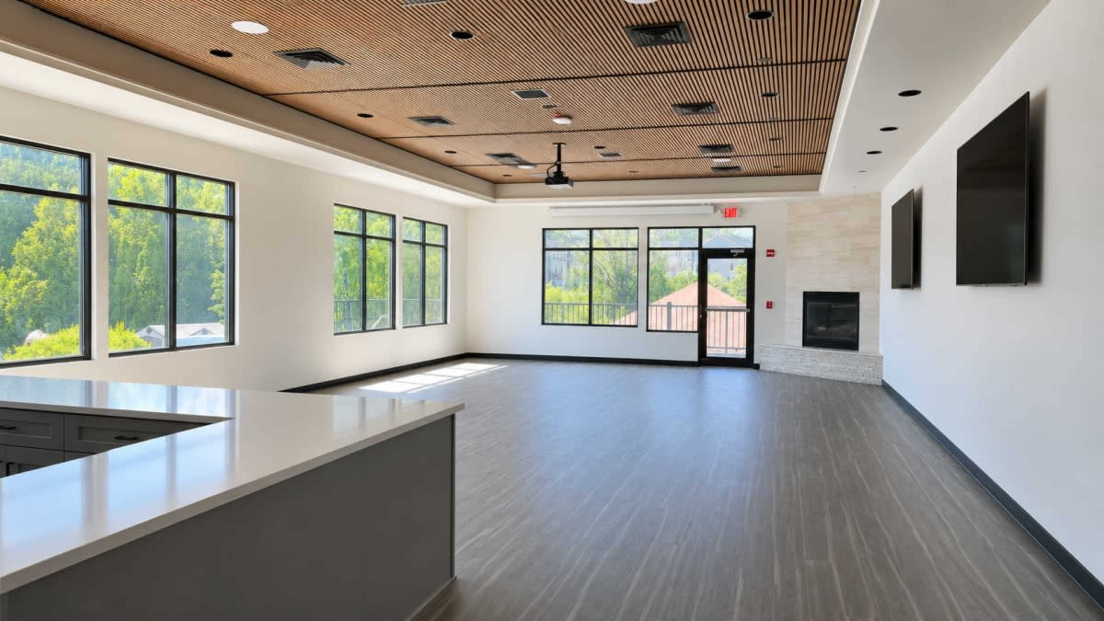 The image shows an empty modern interior space with large windows, a kitchenette area, and a fireplace.