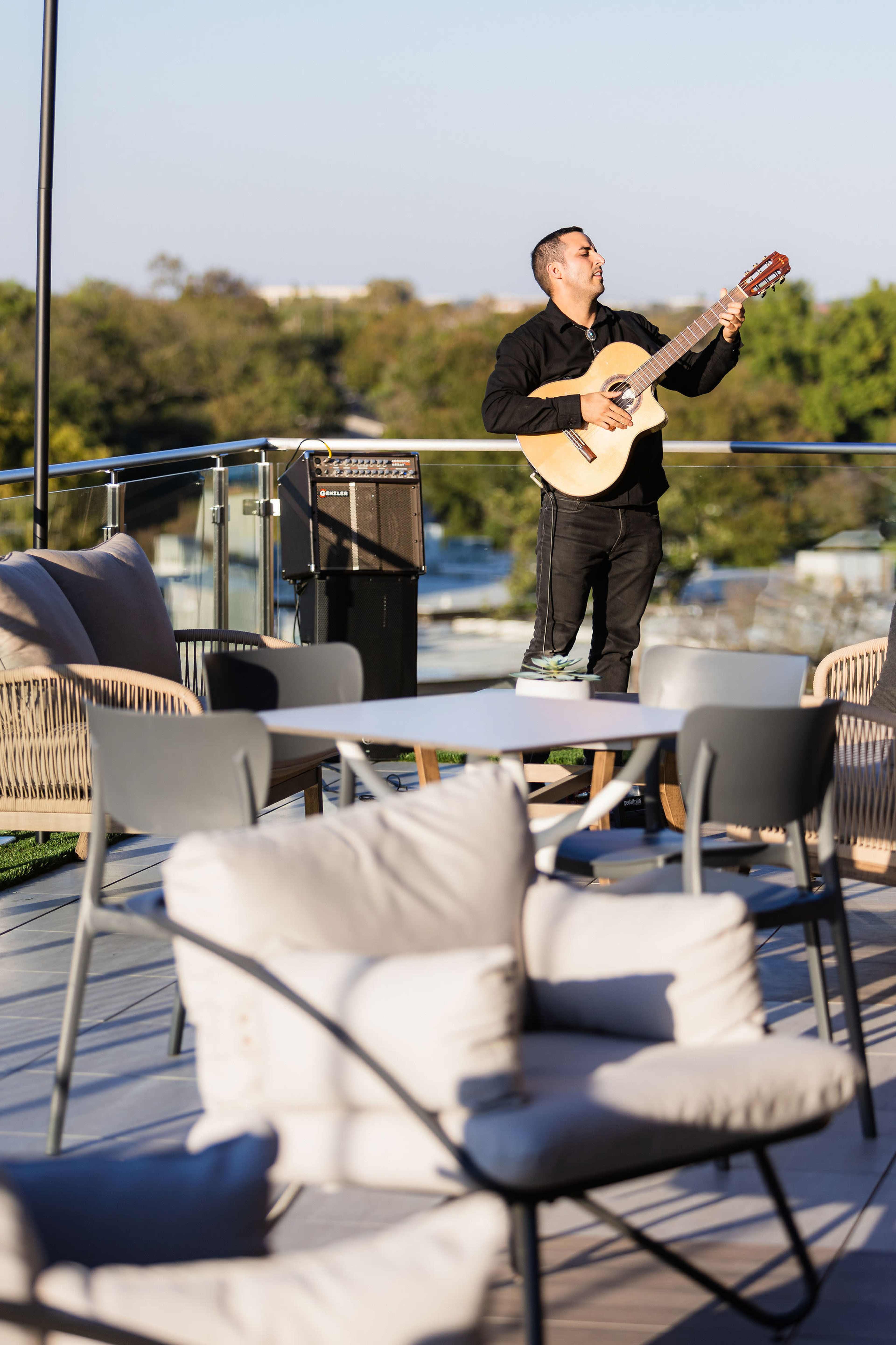 A musician plays a guitar on a rooftop patio surrounded by outdoor furniture.