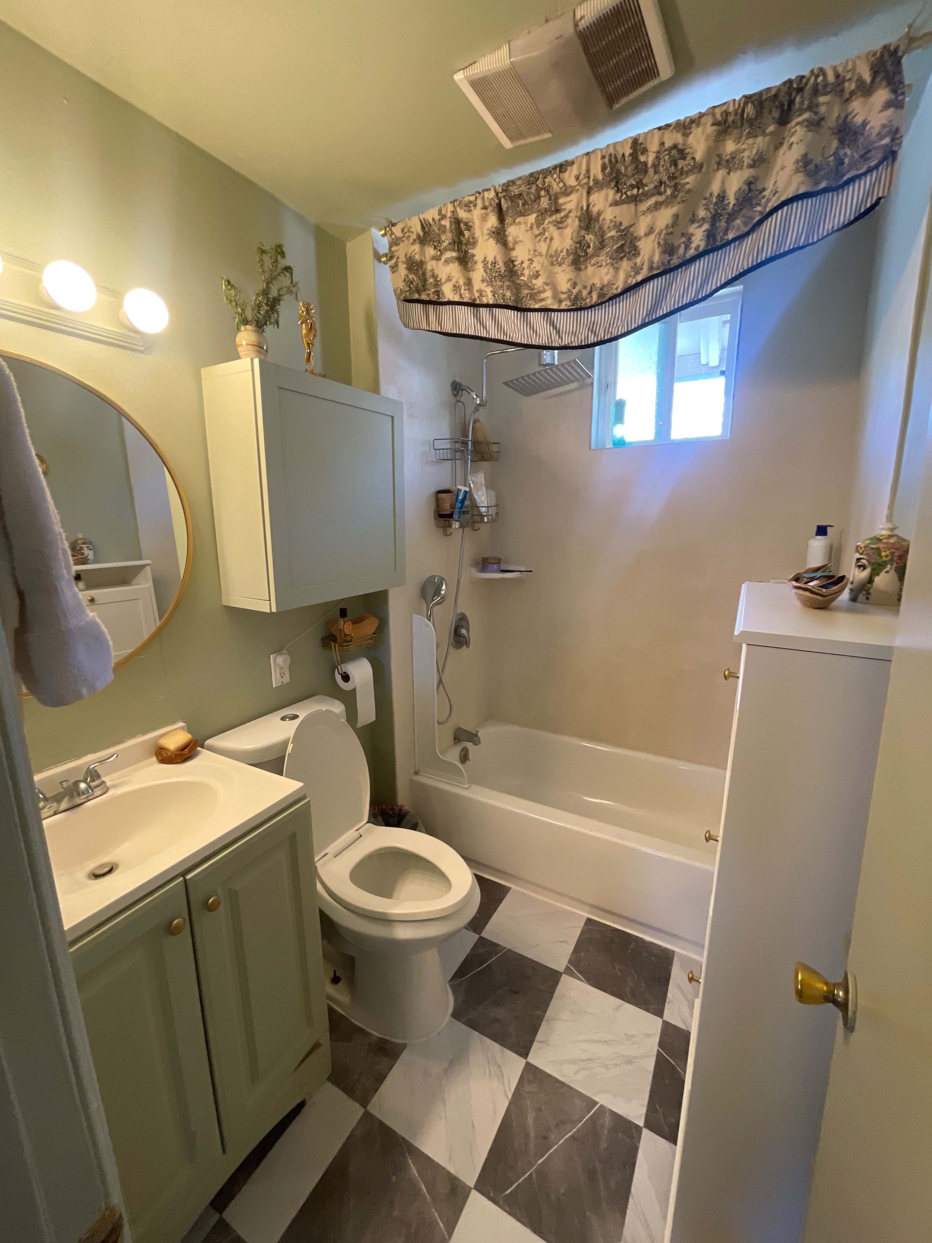 The image shows a small bathroom featuring a bathtub, a toilet, a sink with a vanity, and patterned tiles on the floor.