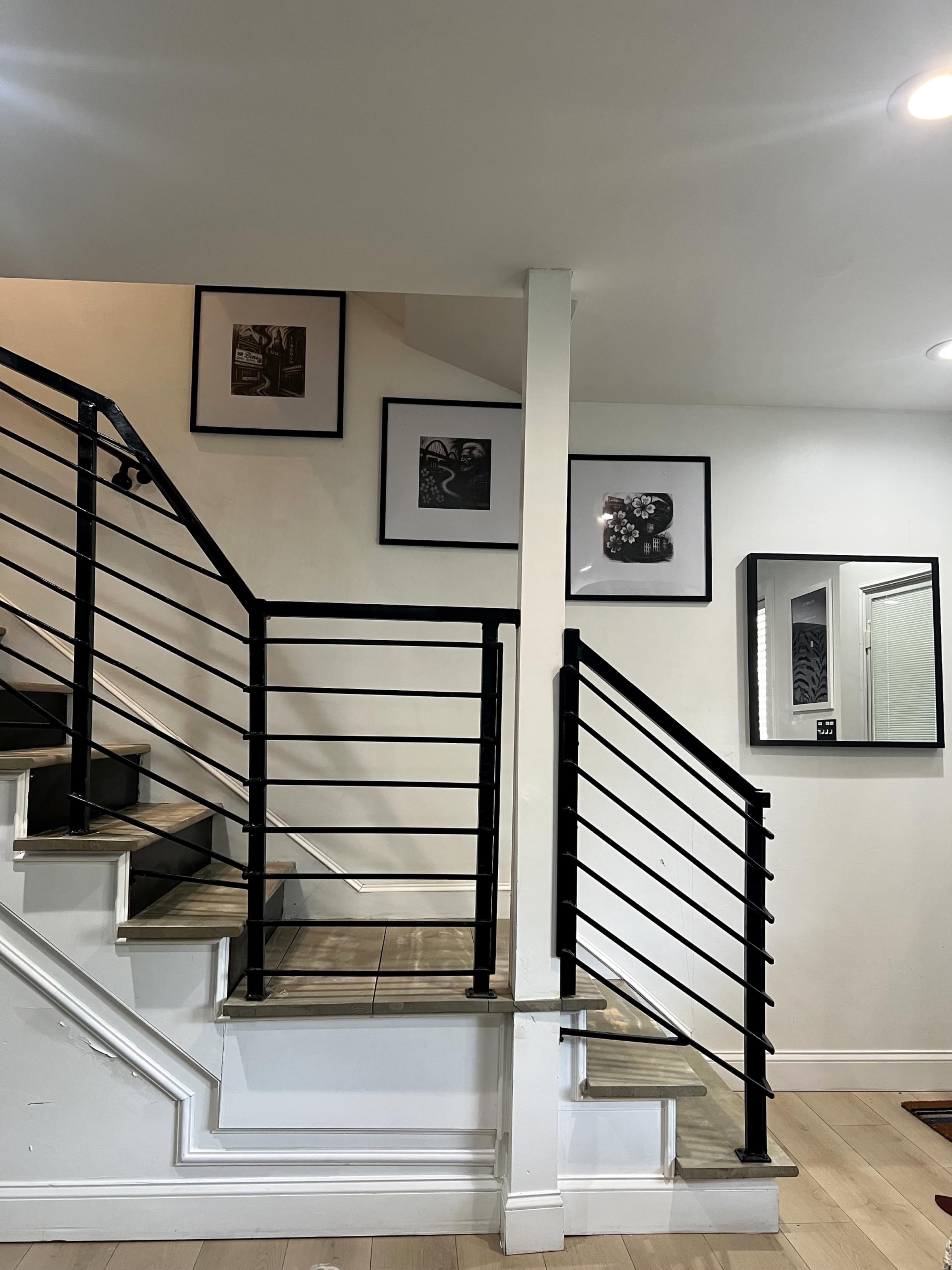The image shows a staircase with black railings and framed black-and-white photos on the wall.