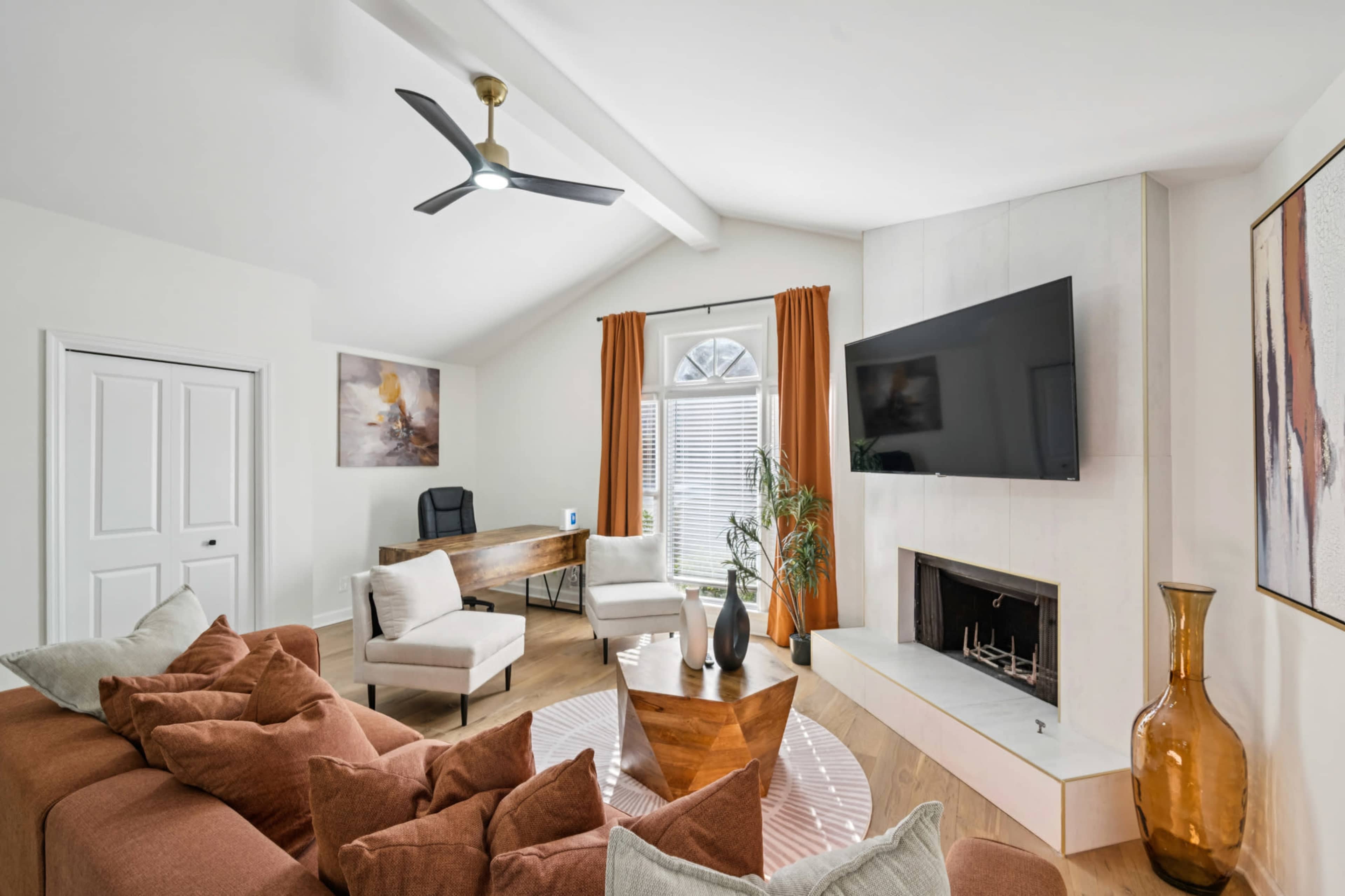 The image shows a modern living room with a large brown sectional sofa, a glass coffee table, and a desk in the background, featuring a mounted television and a decorative vase.