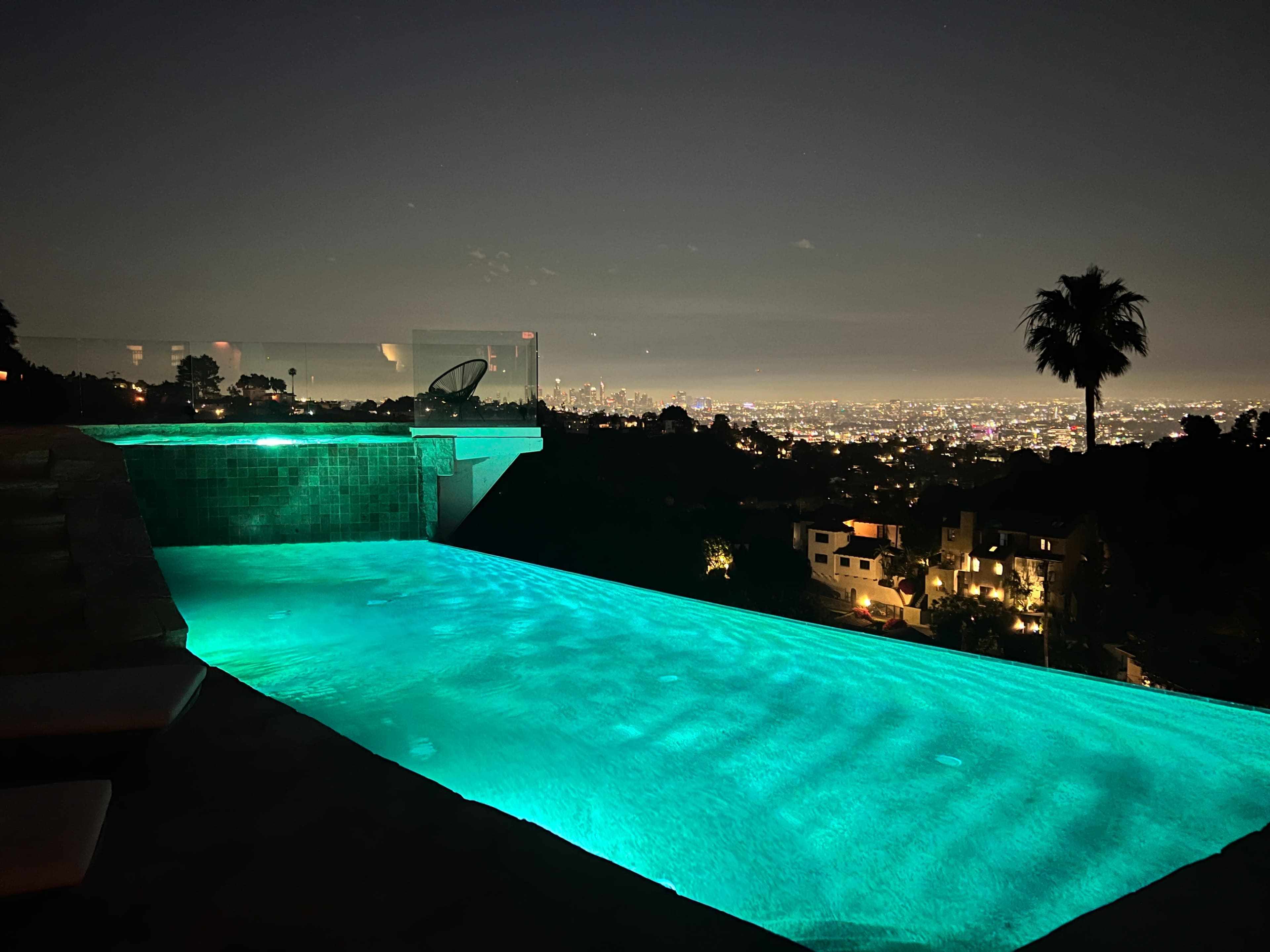A illuminated infinity pool overlooks a city skyline at night.