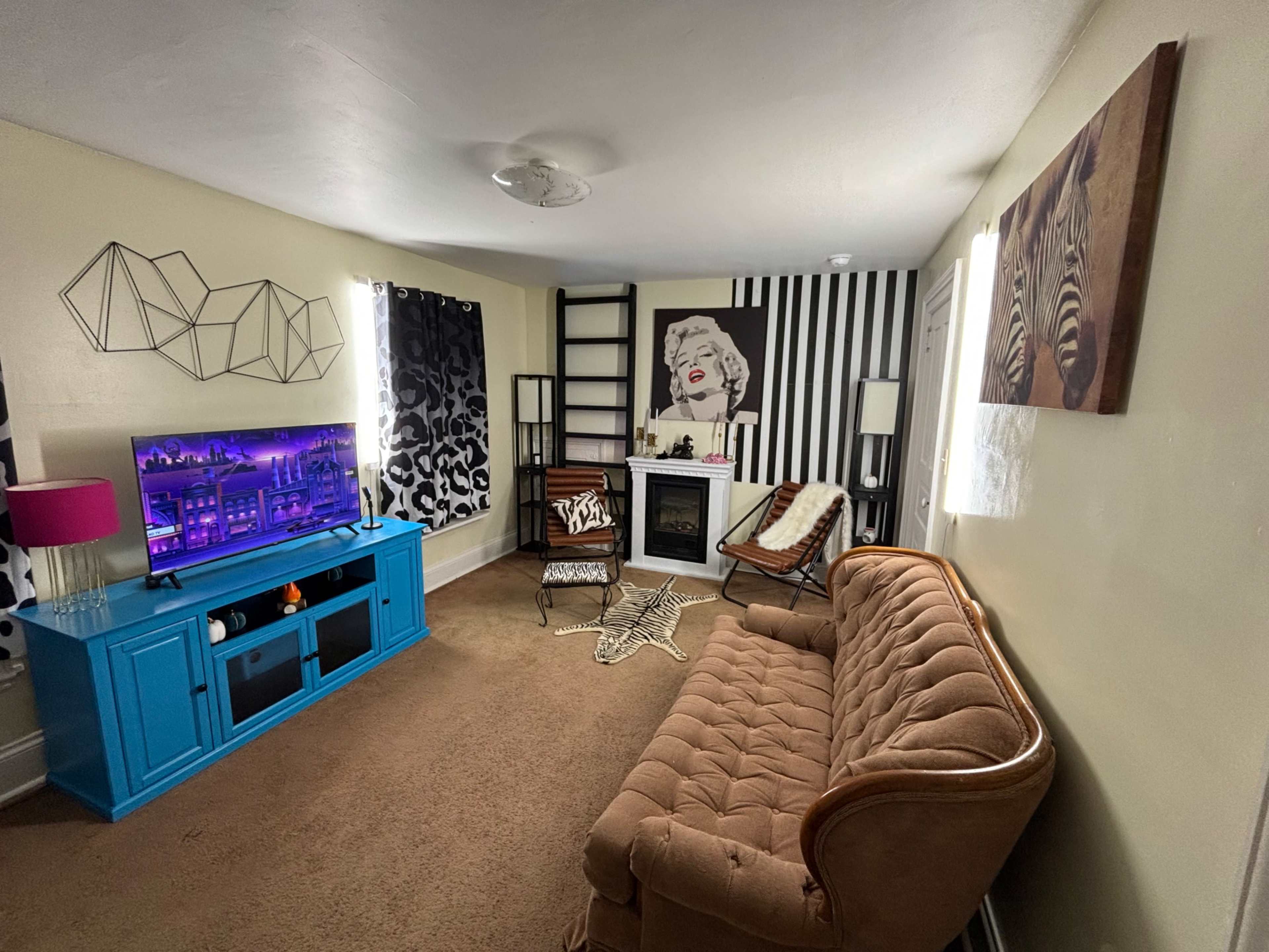 The image shows a living room with a brown couch, turquoise entertainment unit, and a decorative wall featuring a Marilyn Monroe portrait.