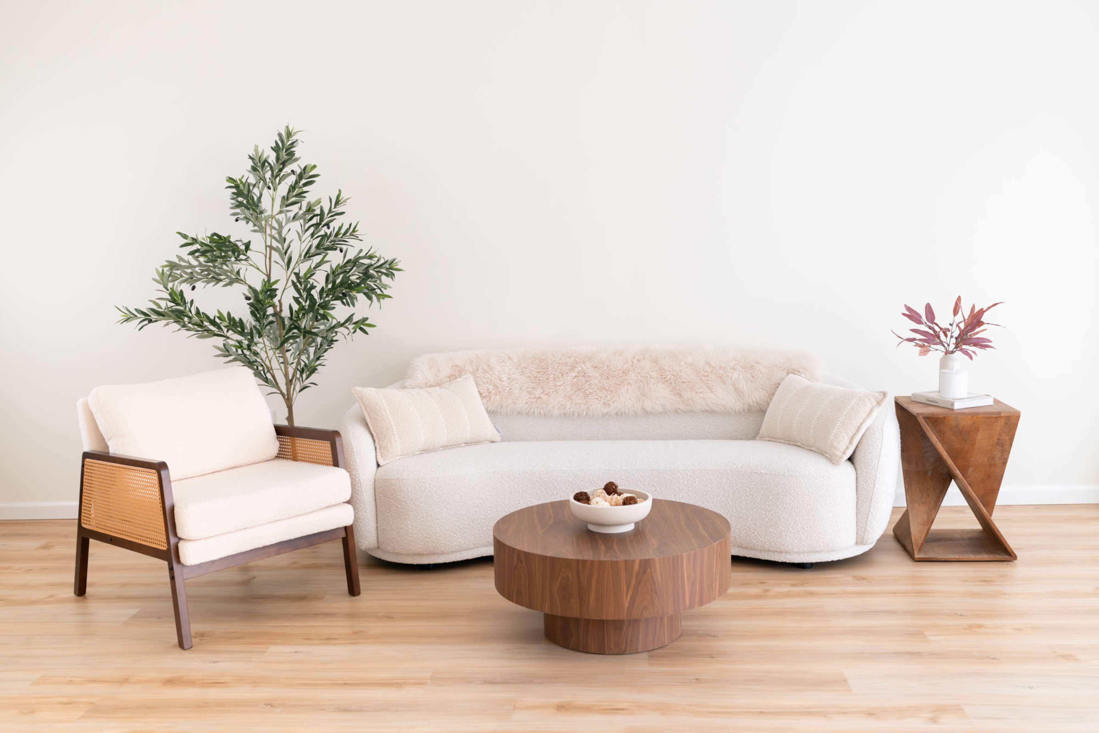 A cozy living room features a plush white sofa, an armchair, a wooden coffee table, and a potted plant against a light-colored wall.