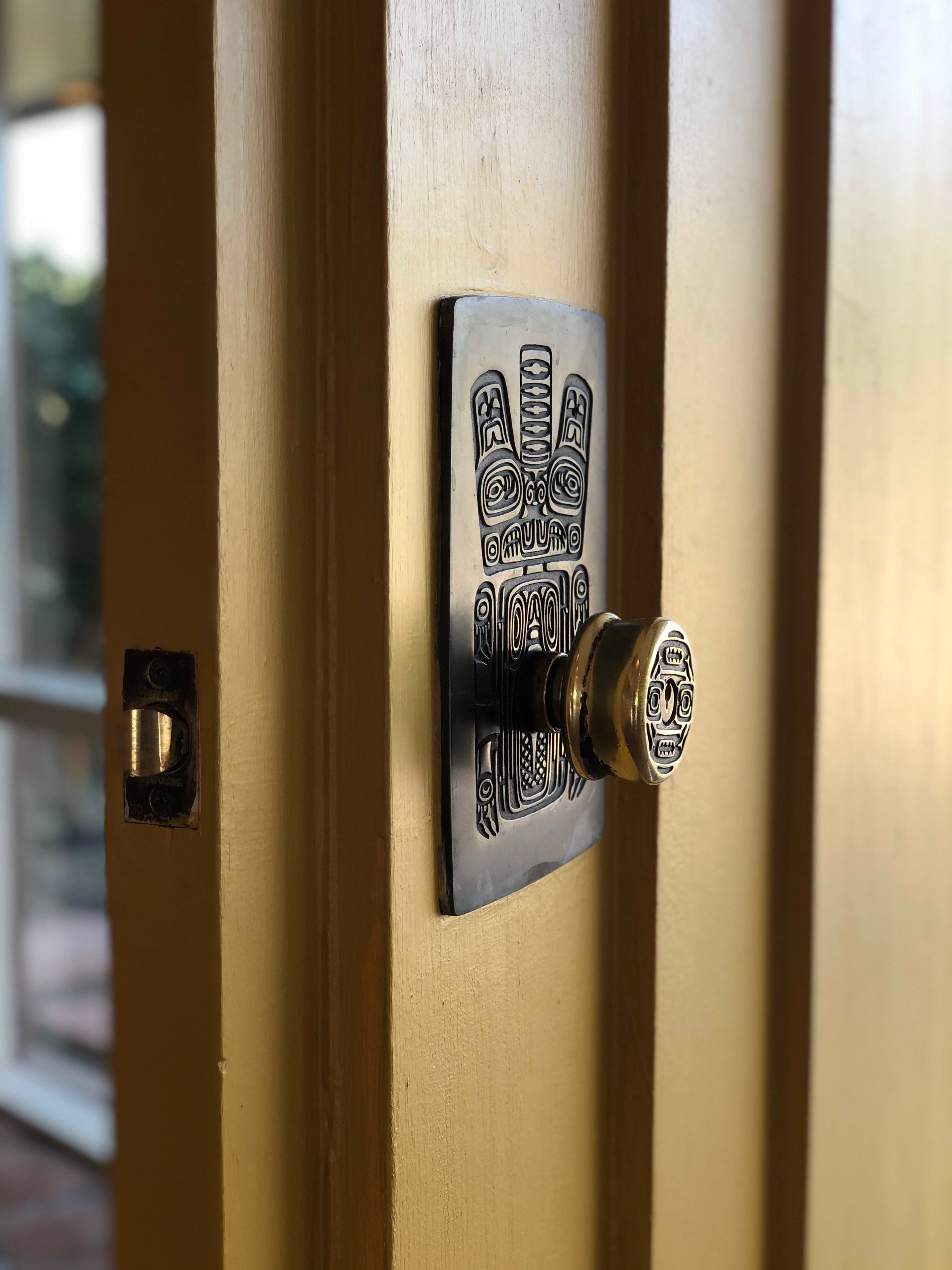 A decorative door handle with intricate patterns mounted on a wooden door.