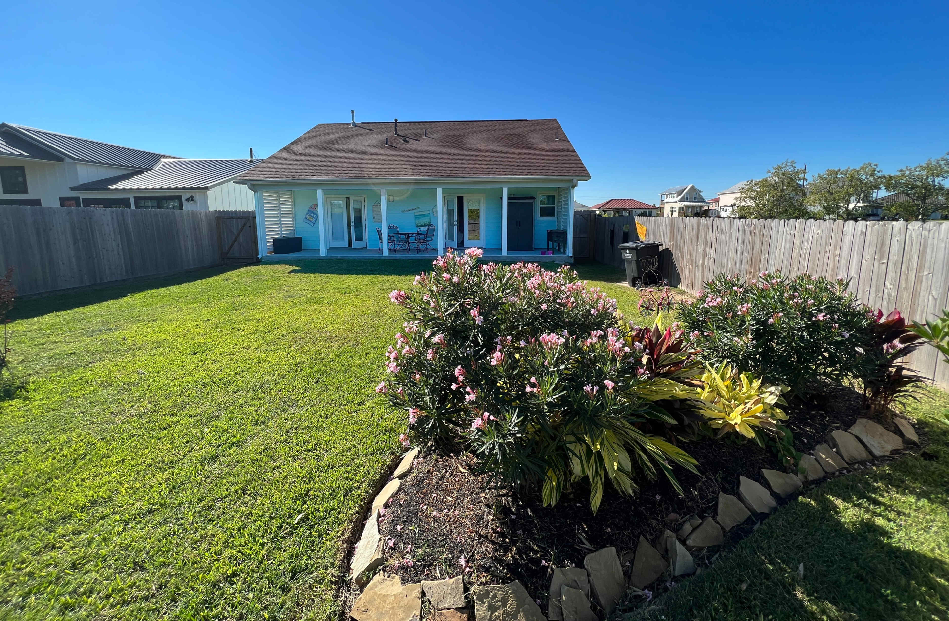 A single-story house with a patio overlooks a well-maintained lawn and flower beds.