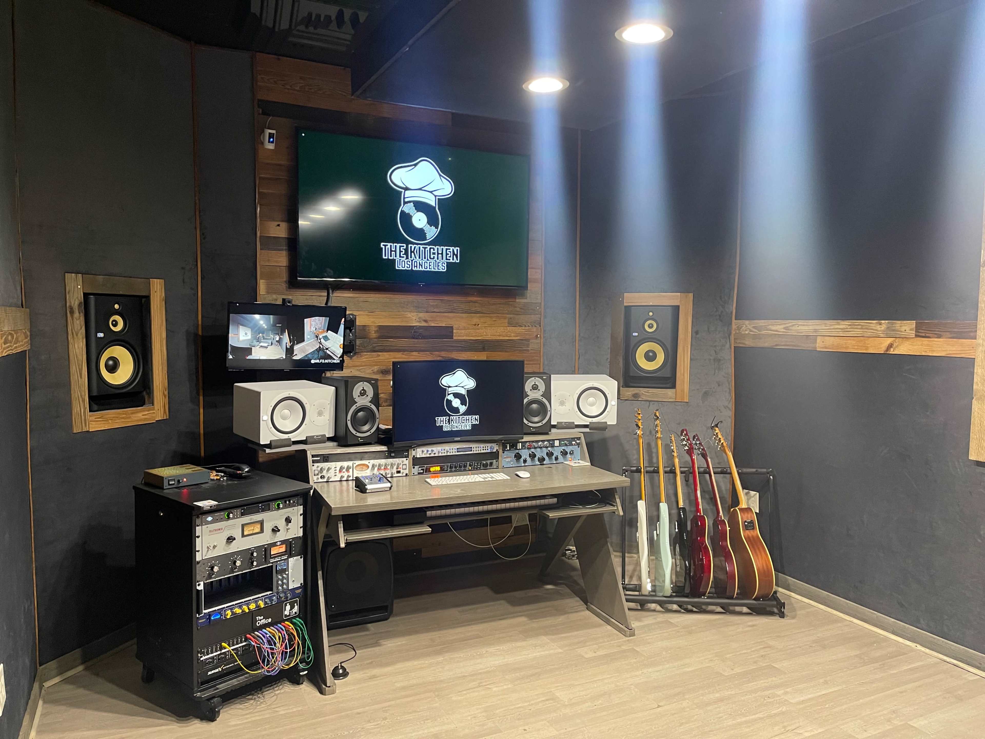 A music studio with a mixing desk, monitors, and various instruments displayed on a rack.