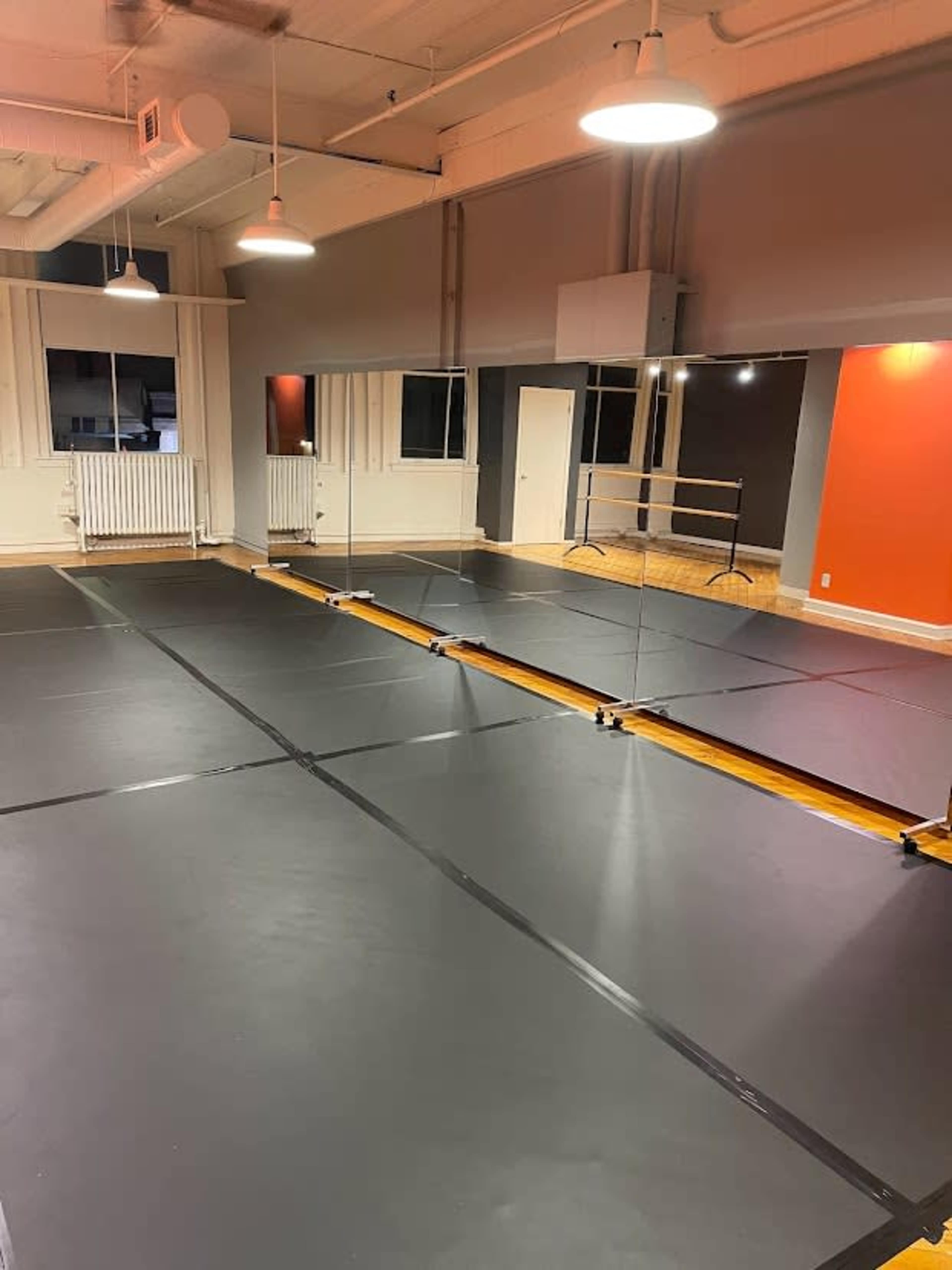 A dance studio with a large mirrored wall and a black rubber floor.
