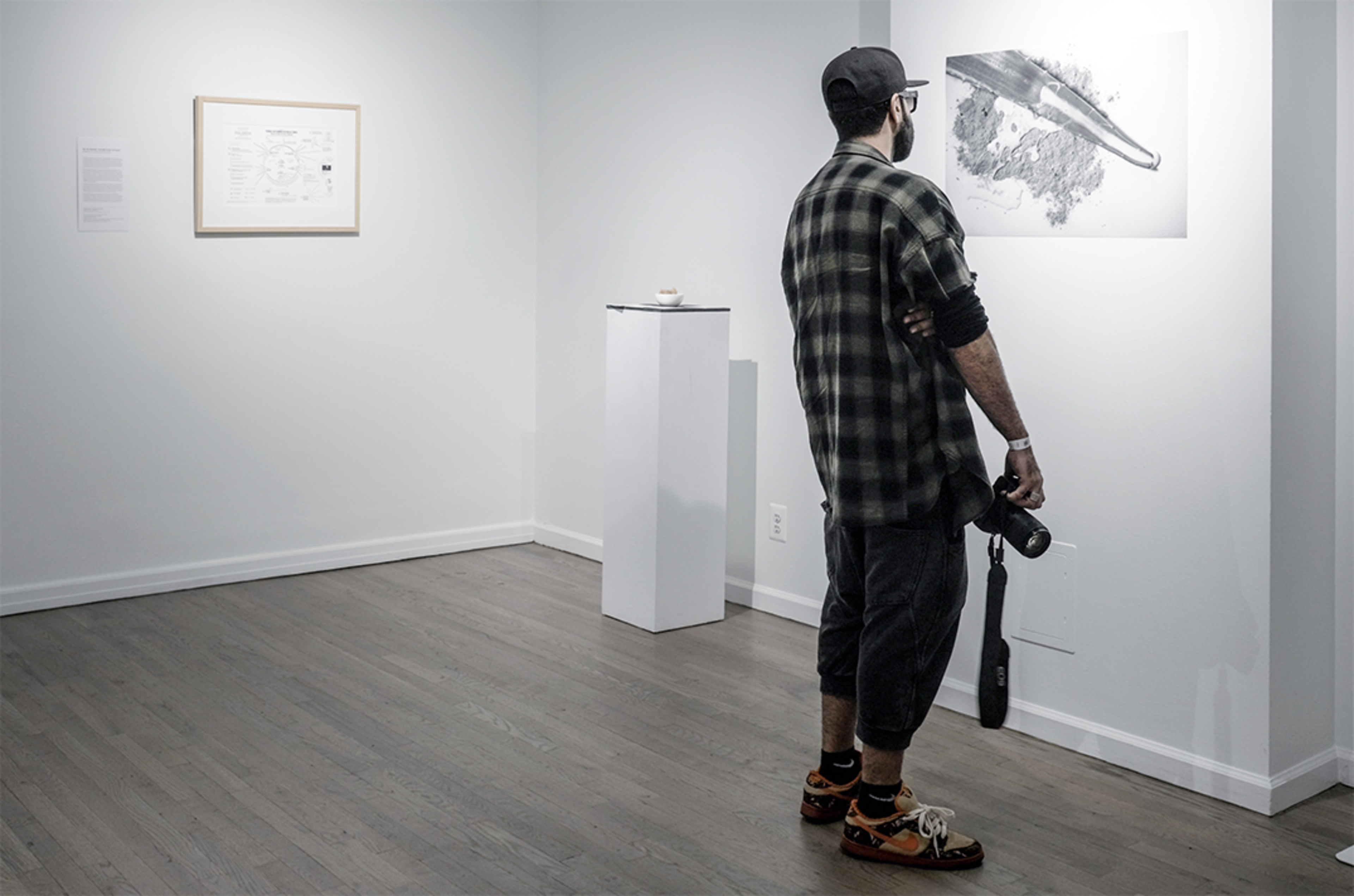 A man stands in an art gallery, observing a large black-and-white photograph of a whale displayed on the wall.