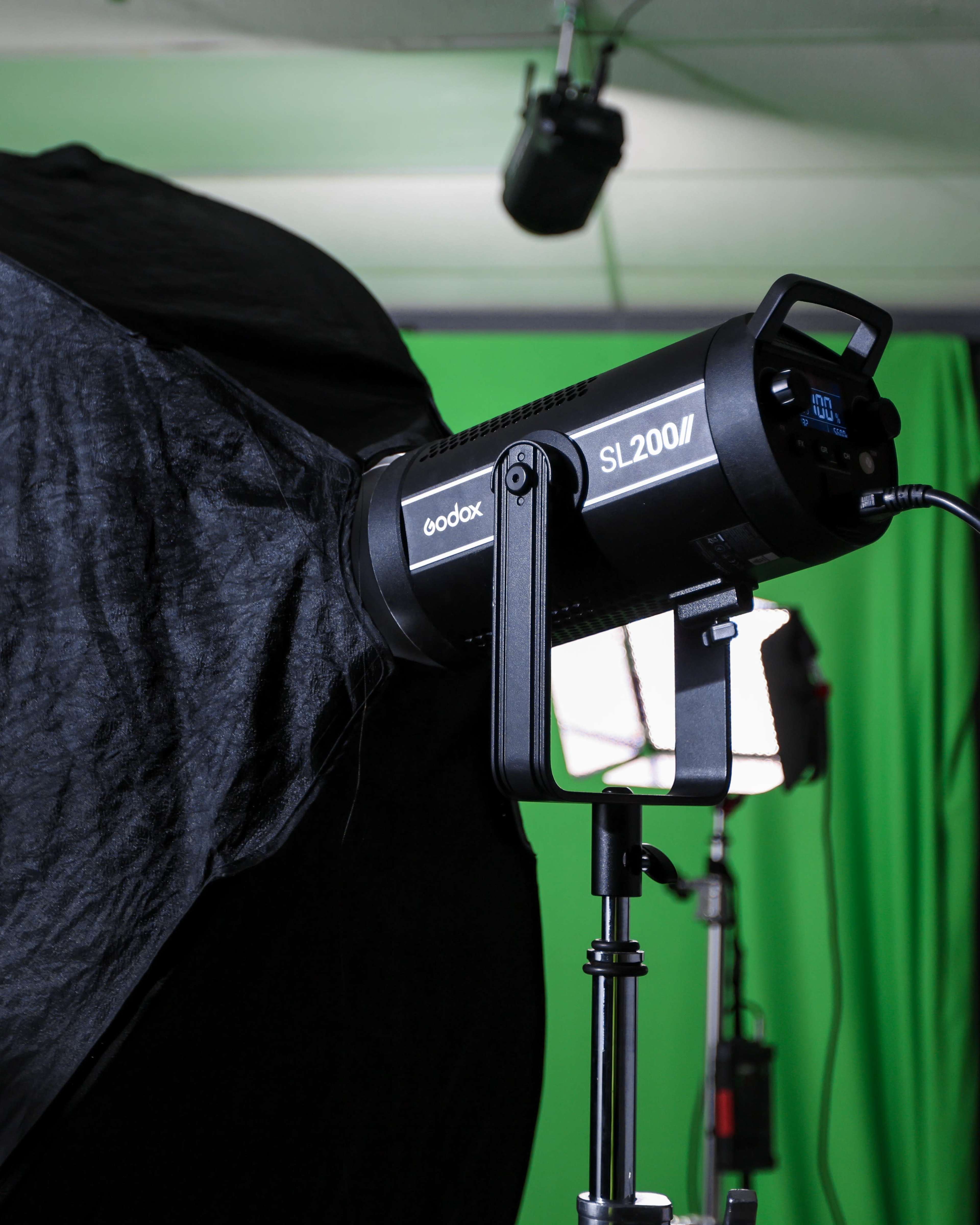 The image shows a Godox SL200II studio light mounted on a stand, partially covered by a black softbox, with a green backdrop behind it.