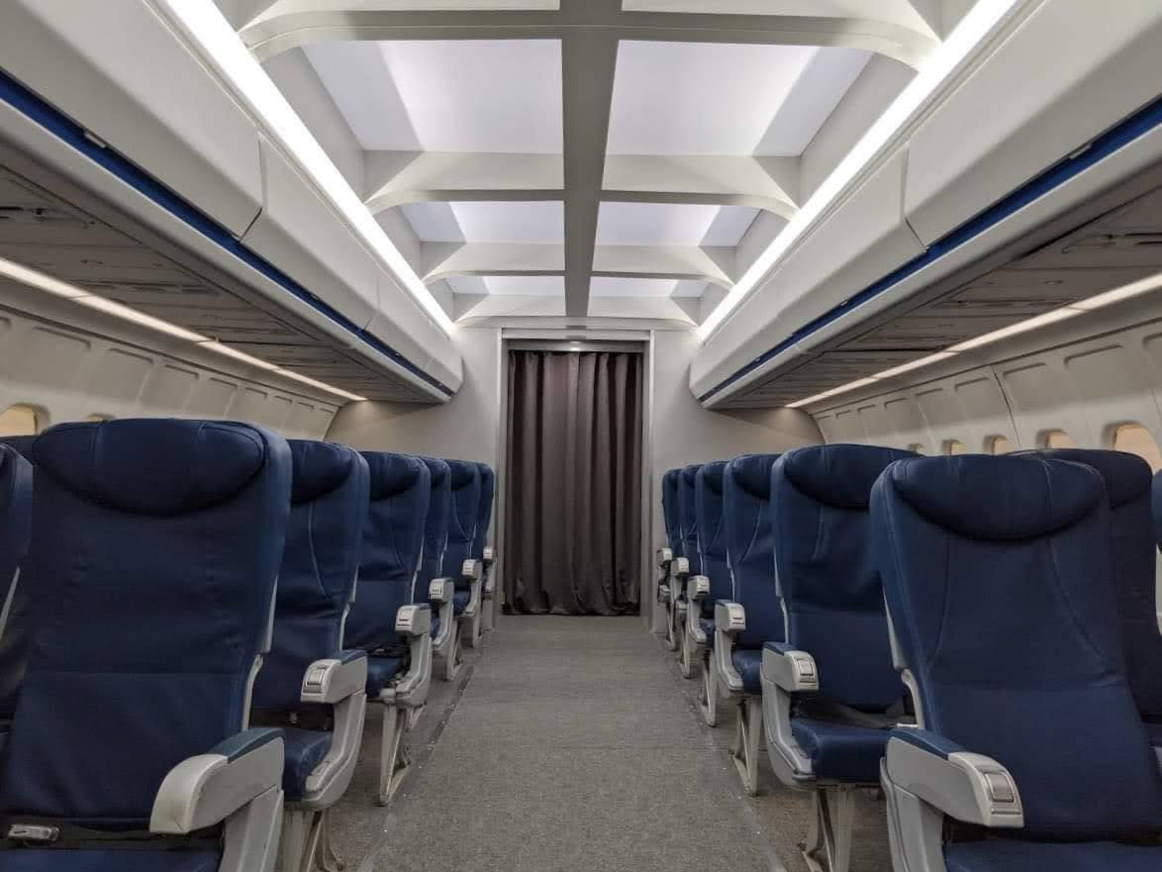 The interior of an airplane cabin with rows of blue upholstered seats and a curtain at the rear.