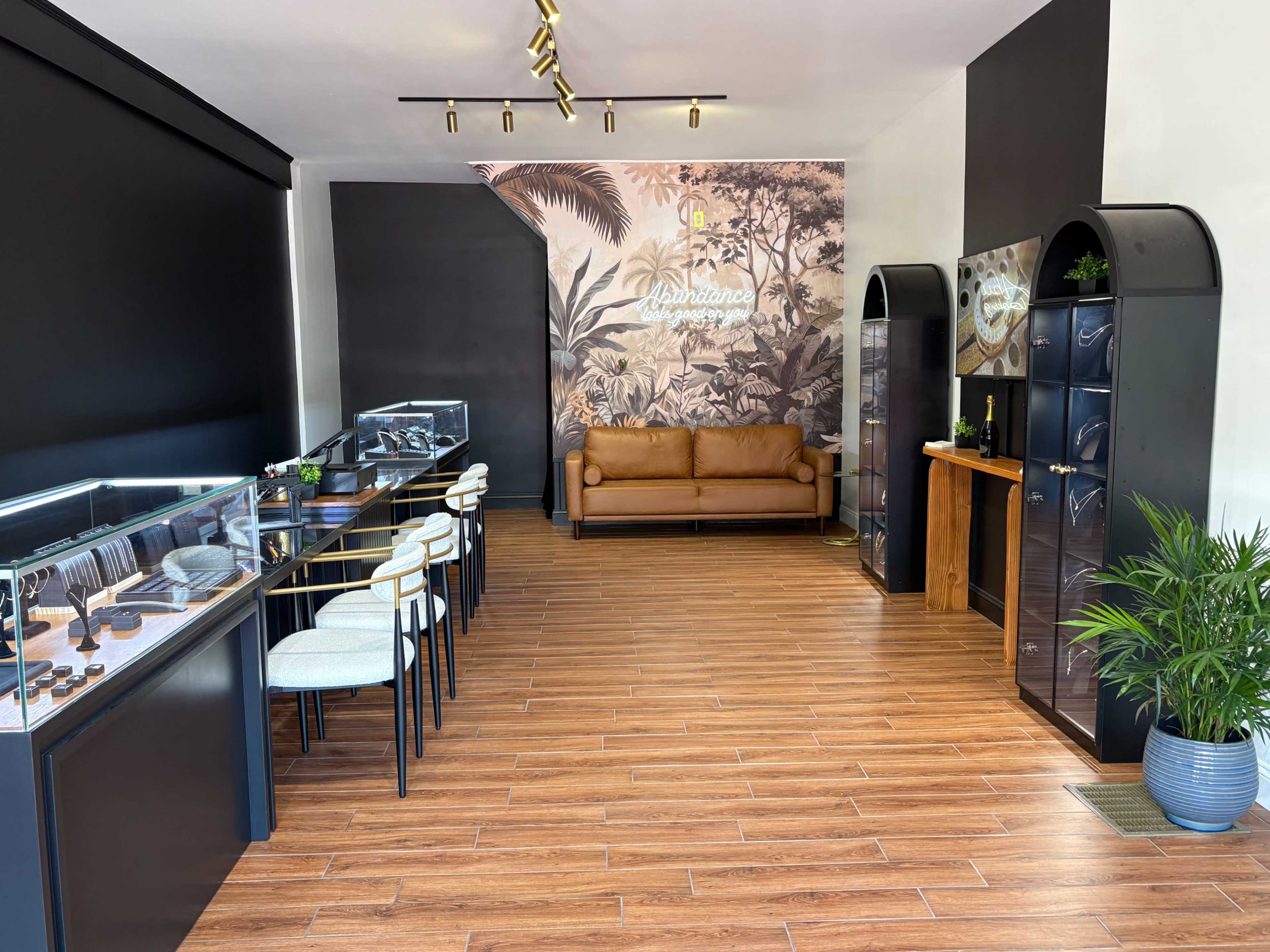 The image shows a jewelry store interior featuring display cases with jewelry, a brown leather couch, and a decorative tropical mural on the wall.