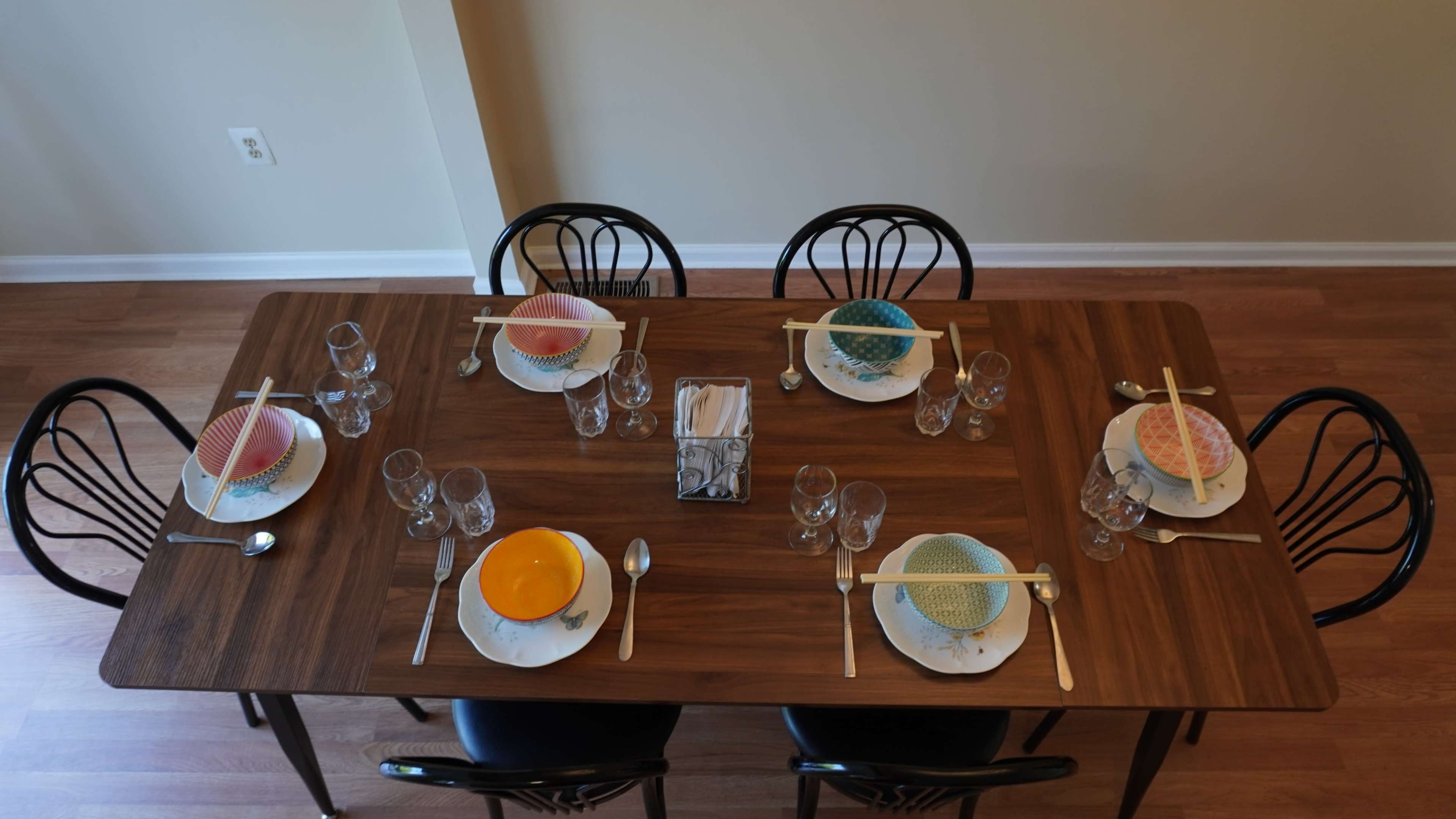 A wooden dining table is set for six, featuring colorful plates and glasses arranged neatly at each place setting.