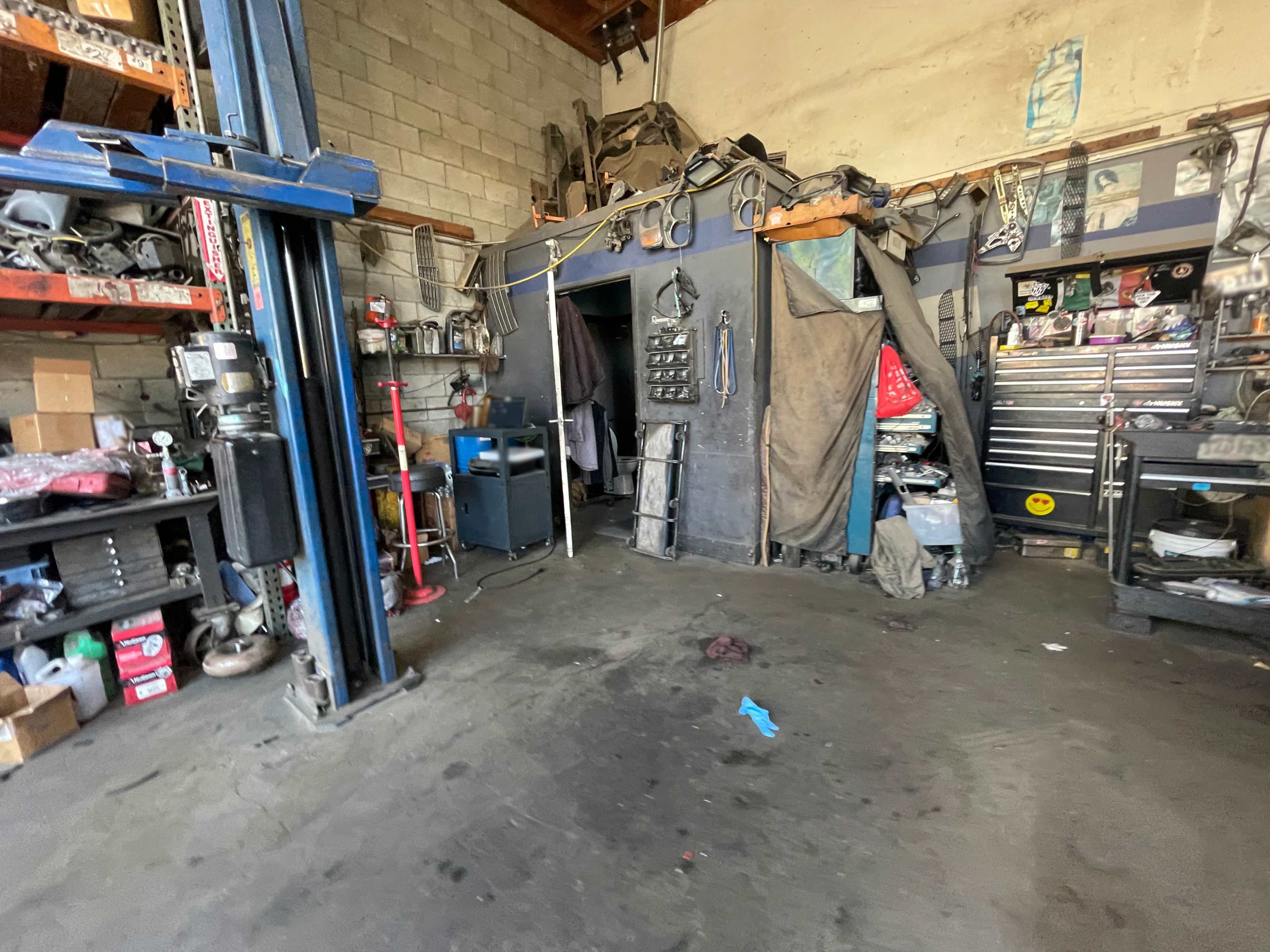 The image shows an automotive workshop with tools, equipment, and a large lift in a cluttered space.