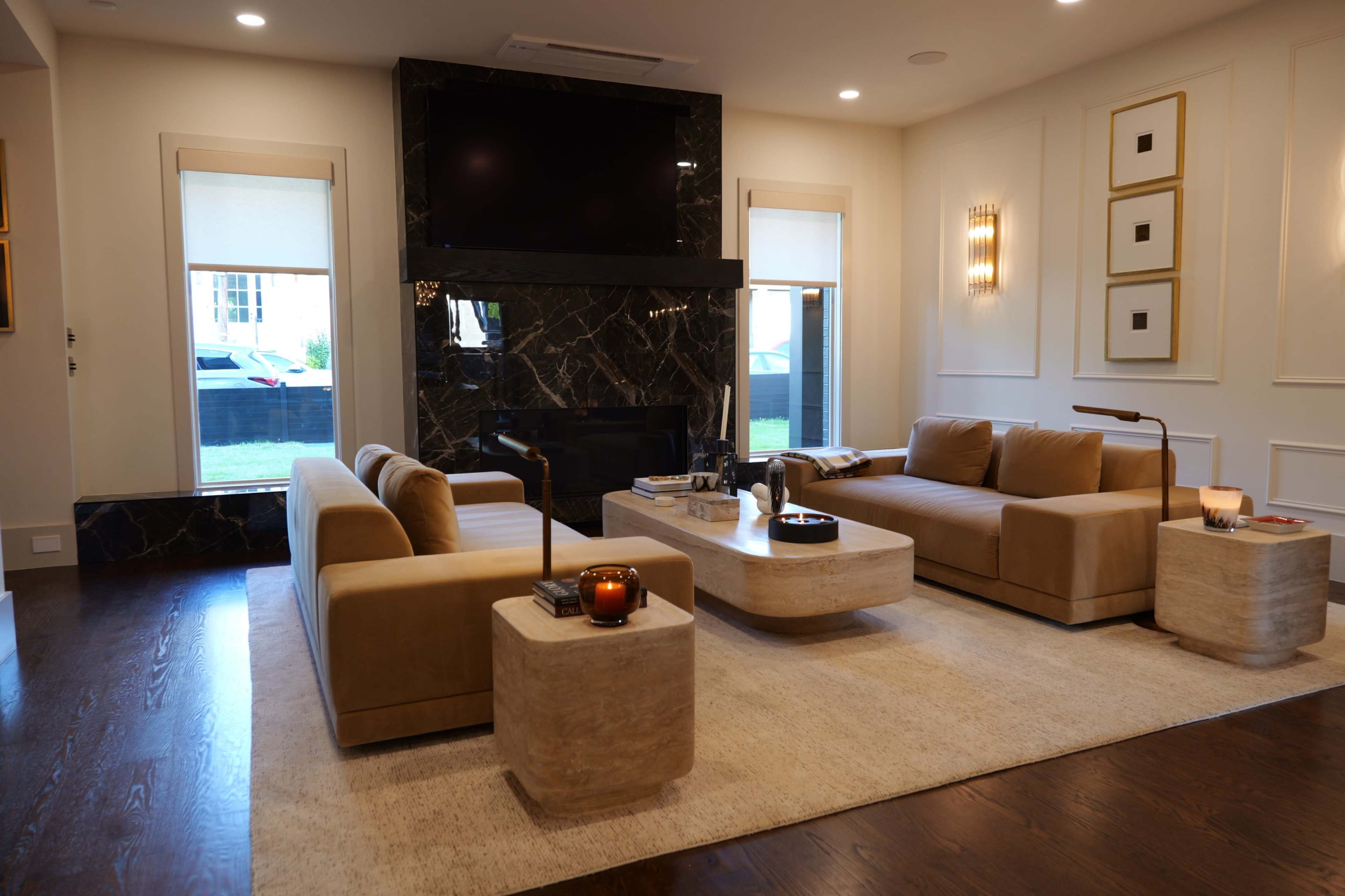 The image shows a modern living room featuring a beige sofa set, a stone coffee table, and a fireplace with a black marble surround.