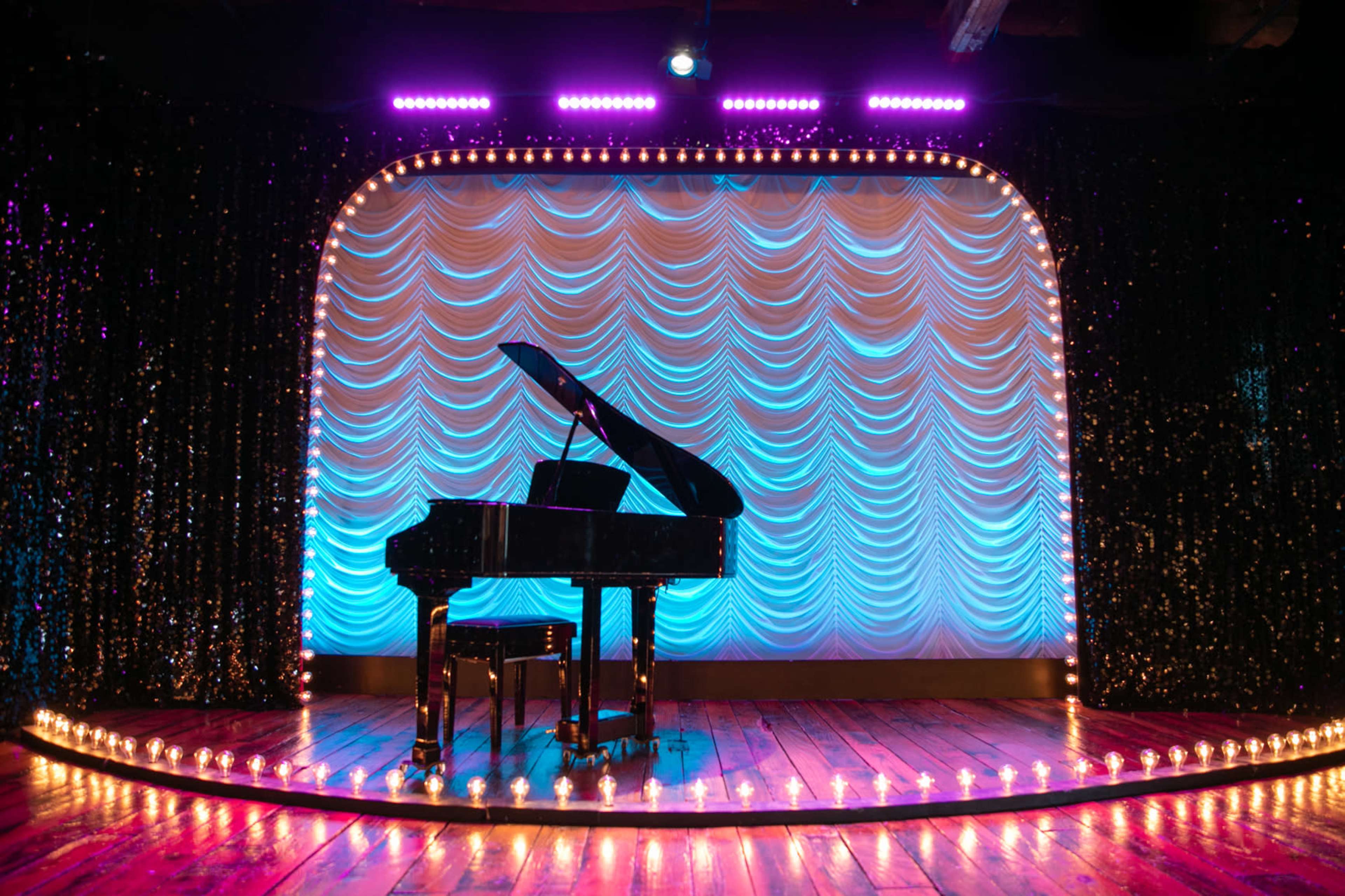 A grand piano sits on a circular stage adorned with lights and a draped backdrop.