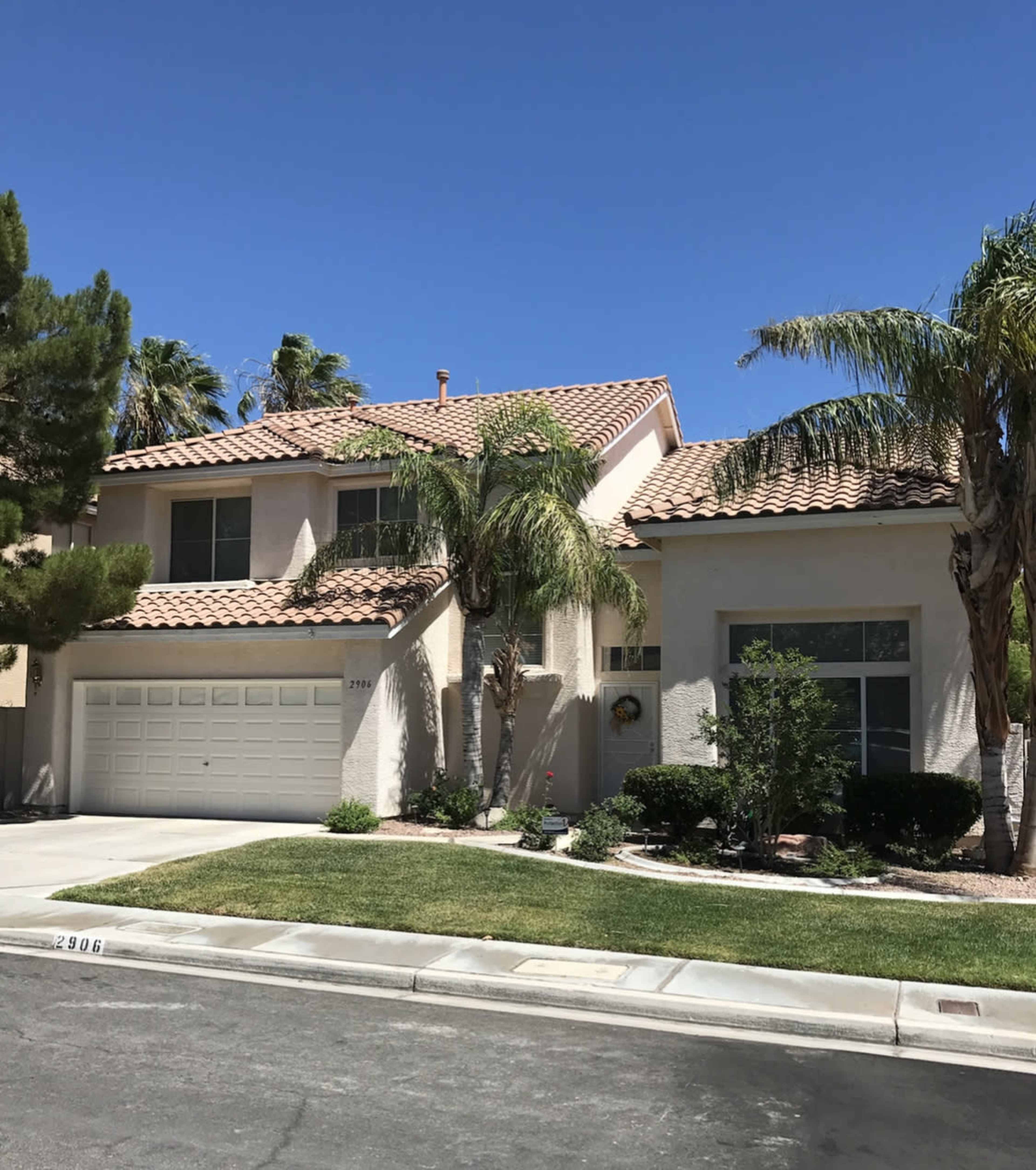 A two-story house with a tile roof and a well-maintained front yard, located on a suburban street.