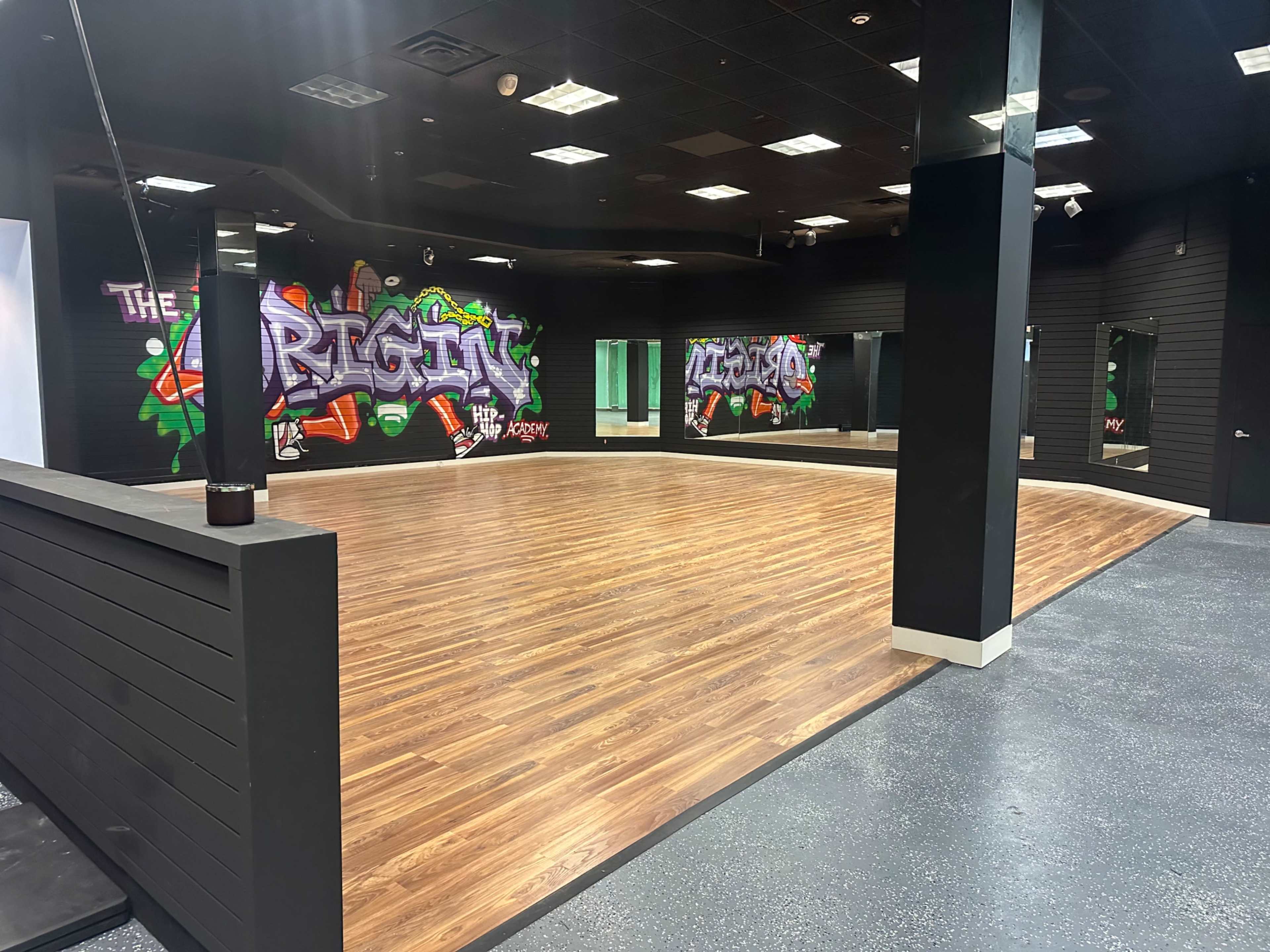 A spacious studio features a polished wooden floor, mirrored walls, and vibrant graffiti art on one side.