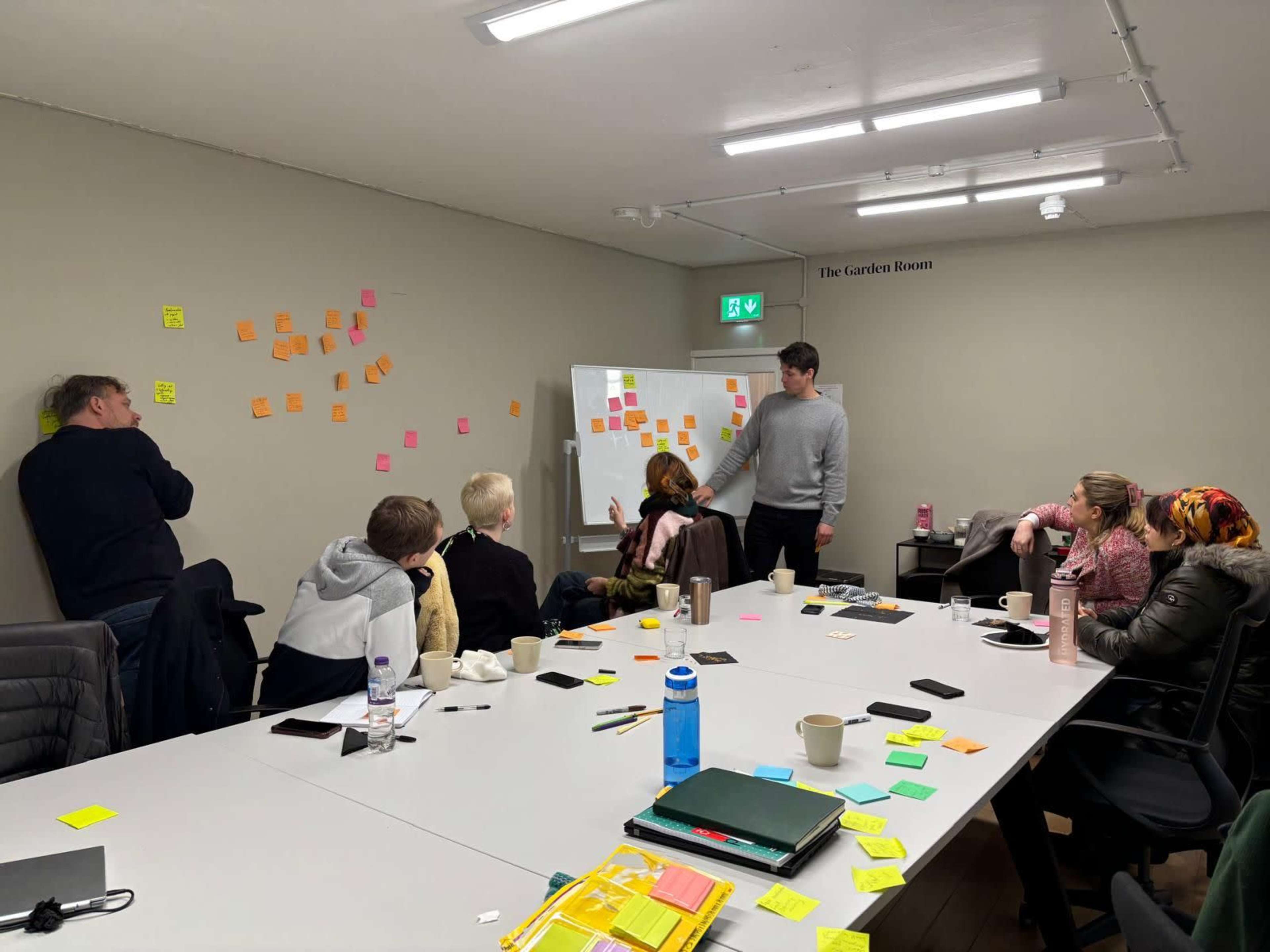 A group of people is gathered in a meeting room, engaged in a brainstorming session with various sticky notes displayed on the walls and a whiteboard.
