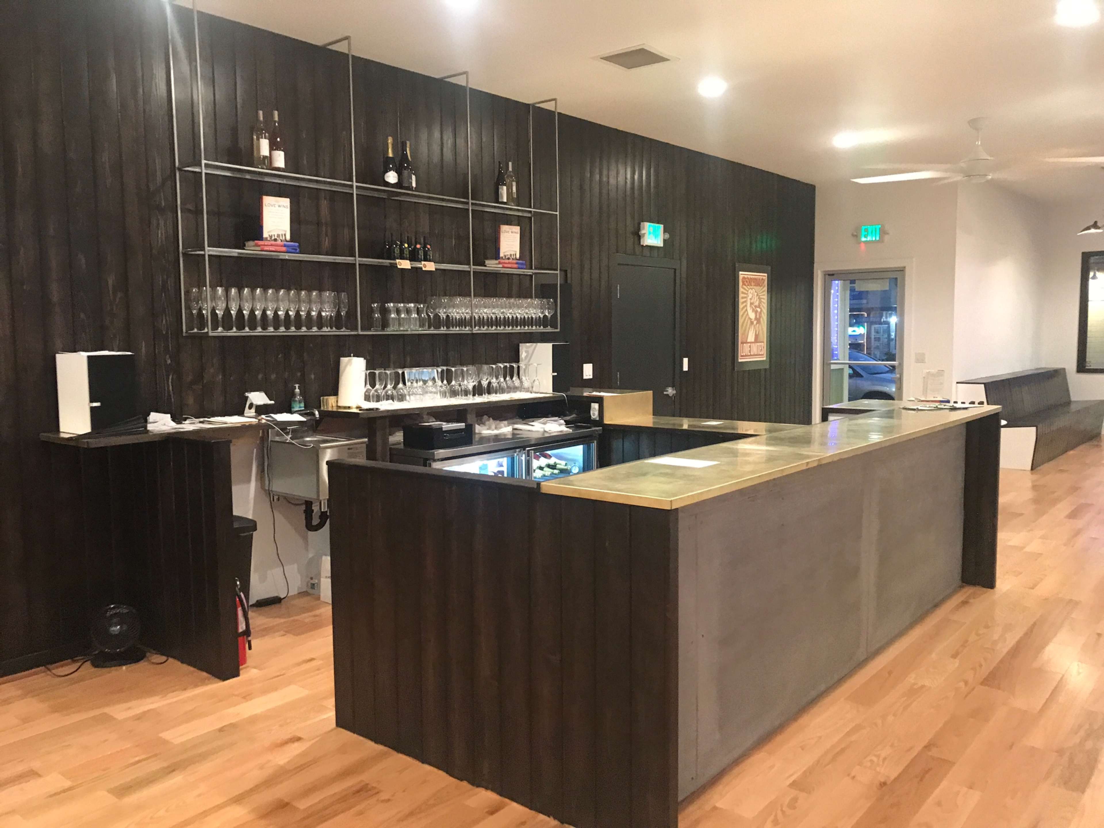 A modern bar area with a concrete counter, wood paneling, shelves for wine bottles, and a display of glasses.