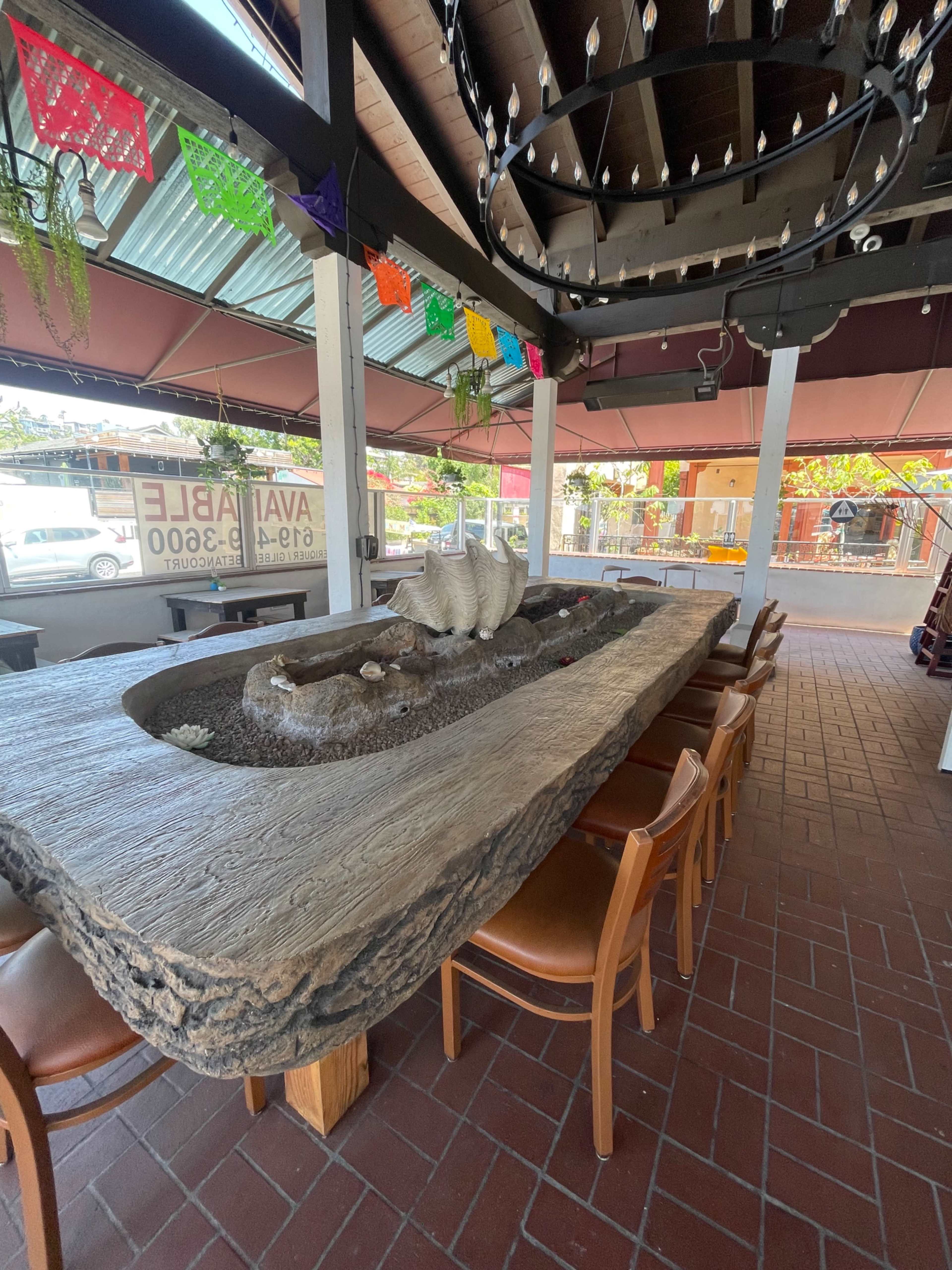 A large, rustic wooden table with a water feature at the center, surrounded by wooden chairs in a restaurant setting.