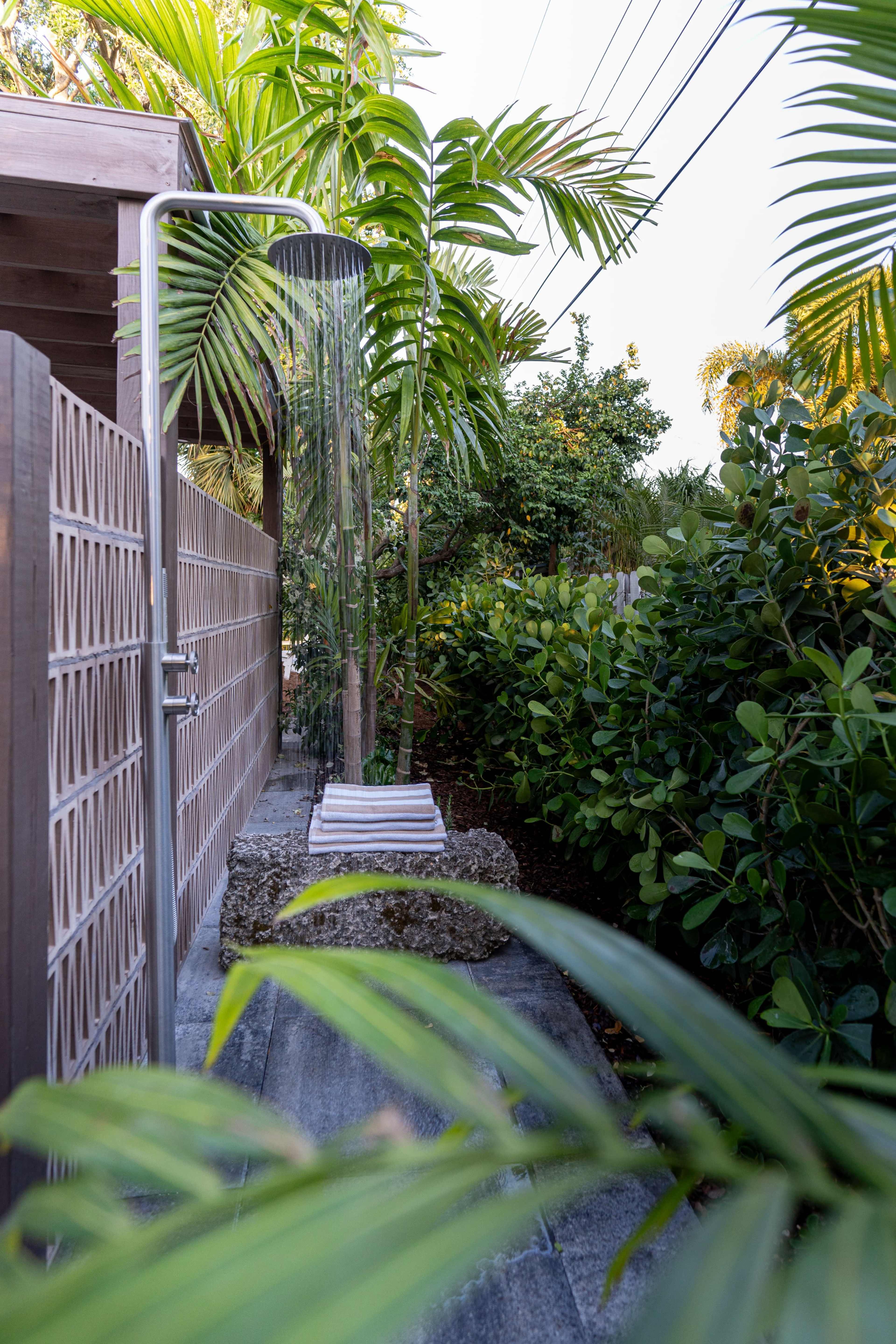 An outdoor shower is positioned beside a pathway surrounded by lush tropical vegetation.