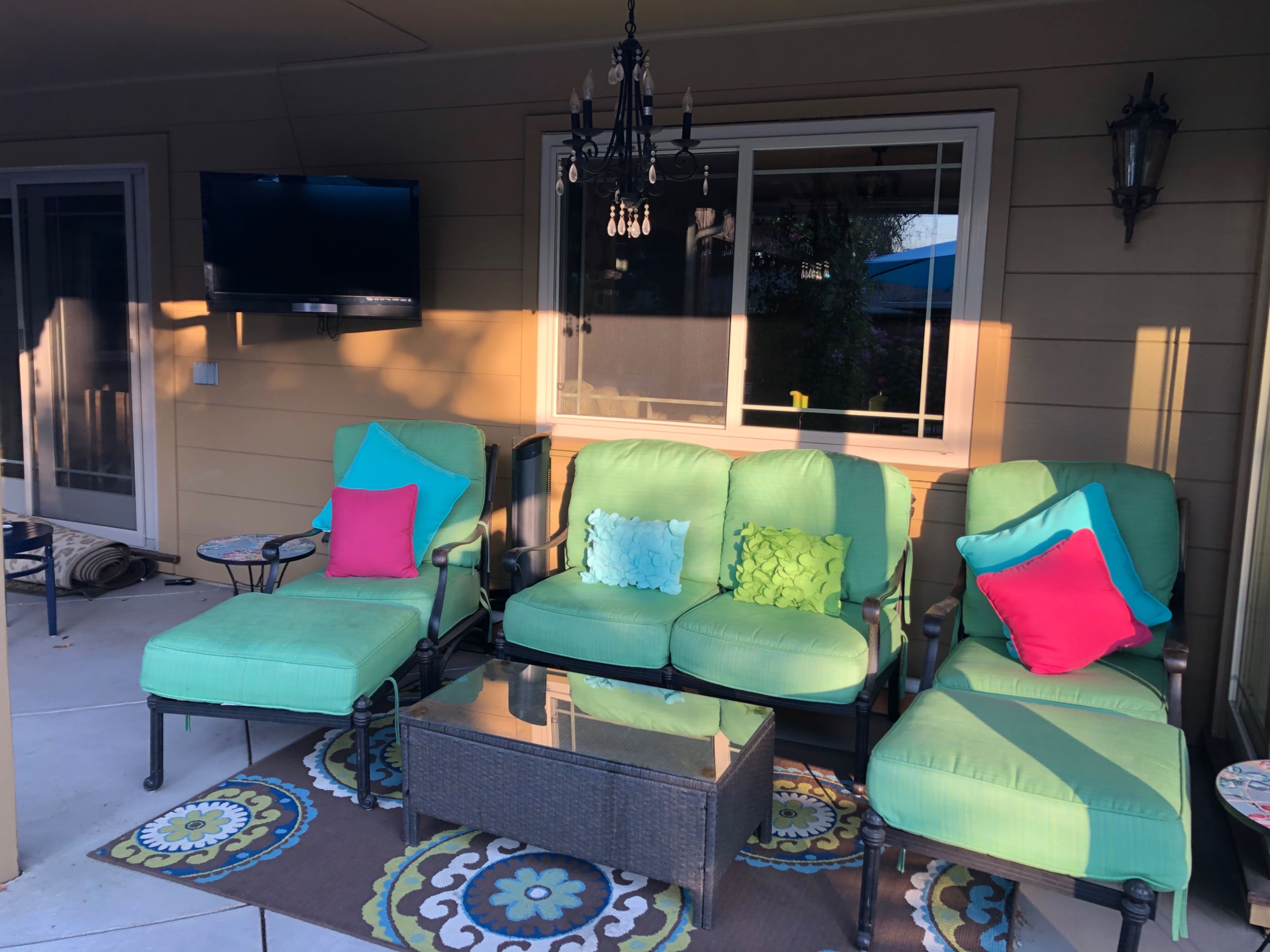 A set of green outdoor furniture with colorful pillows is arranged around a glass coffee table on a patio.