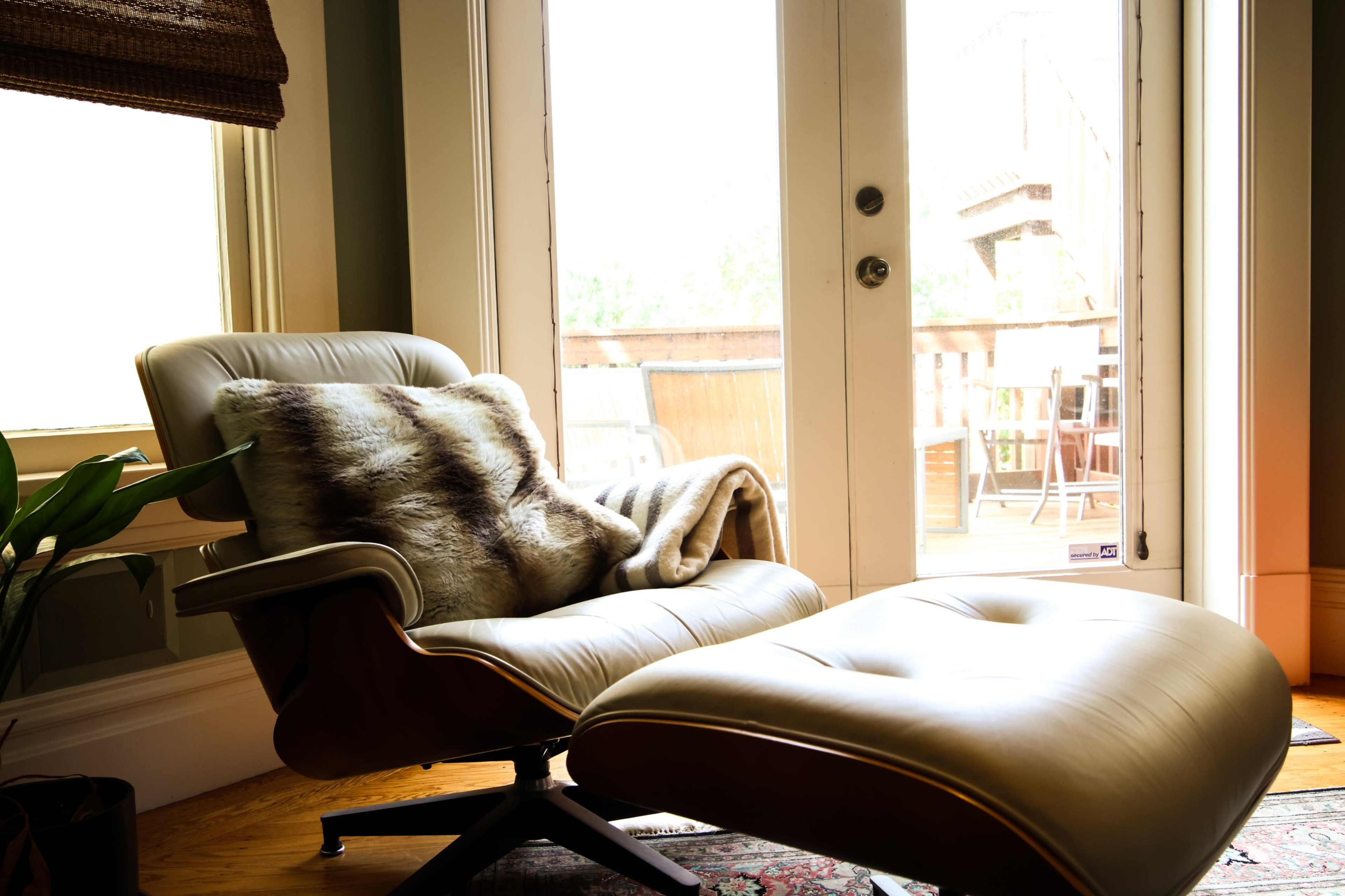 A leather lounge chair with a fur throw is positioned near glass doors that open onto a wooden deck.