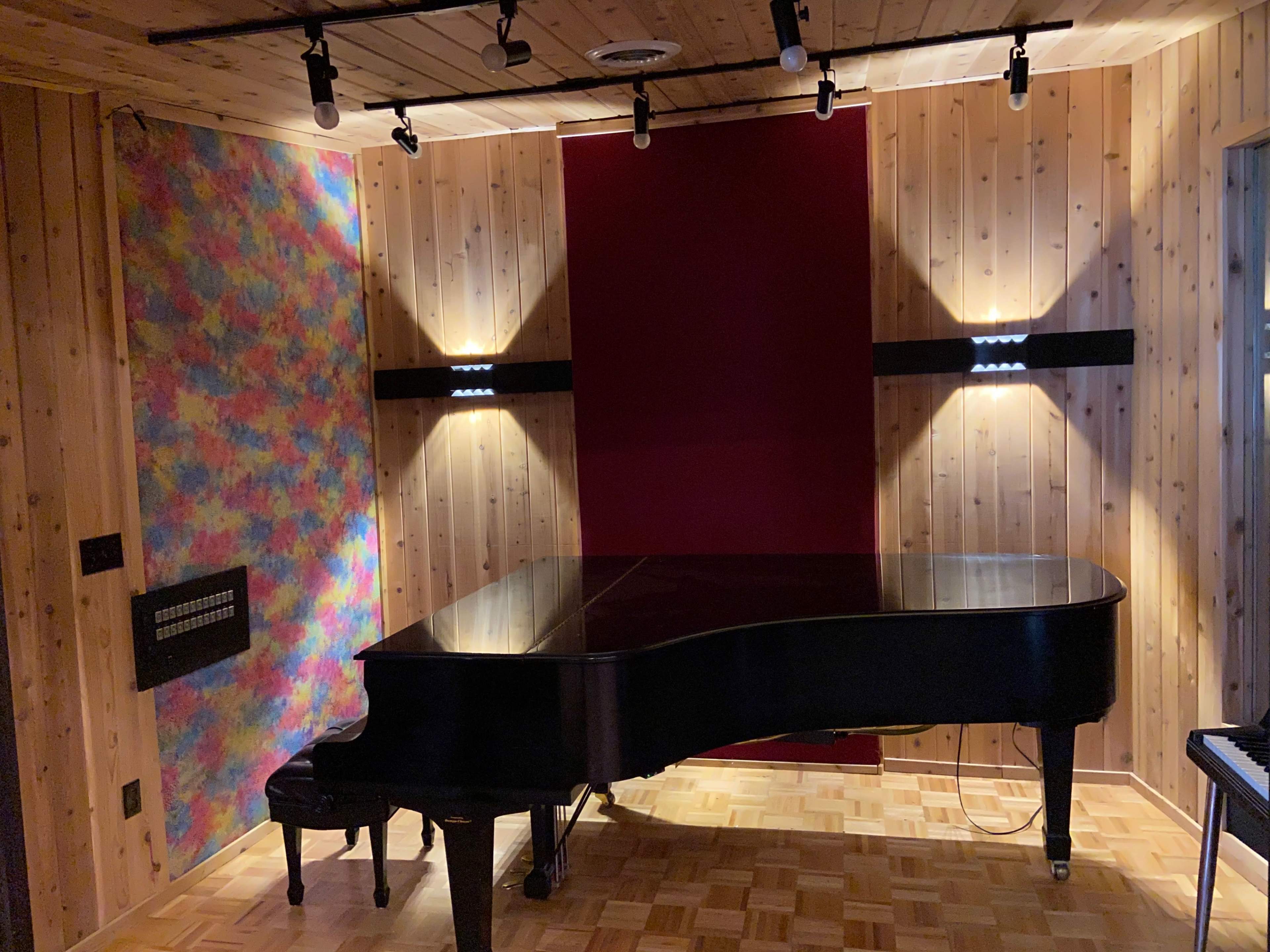 A grand piano positioned in a wooden room with colorful wall accents and ceiling lights.