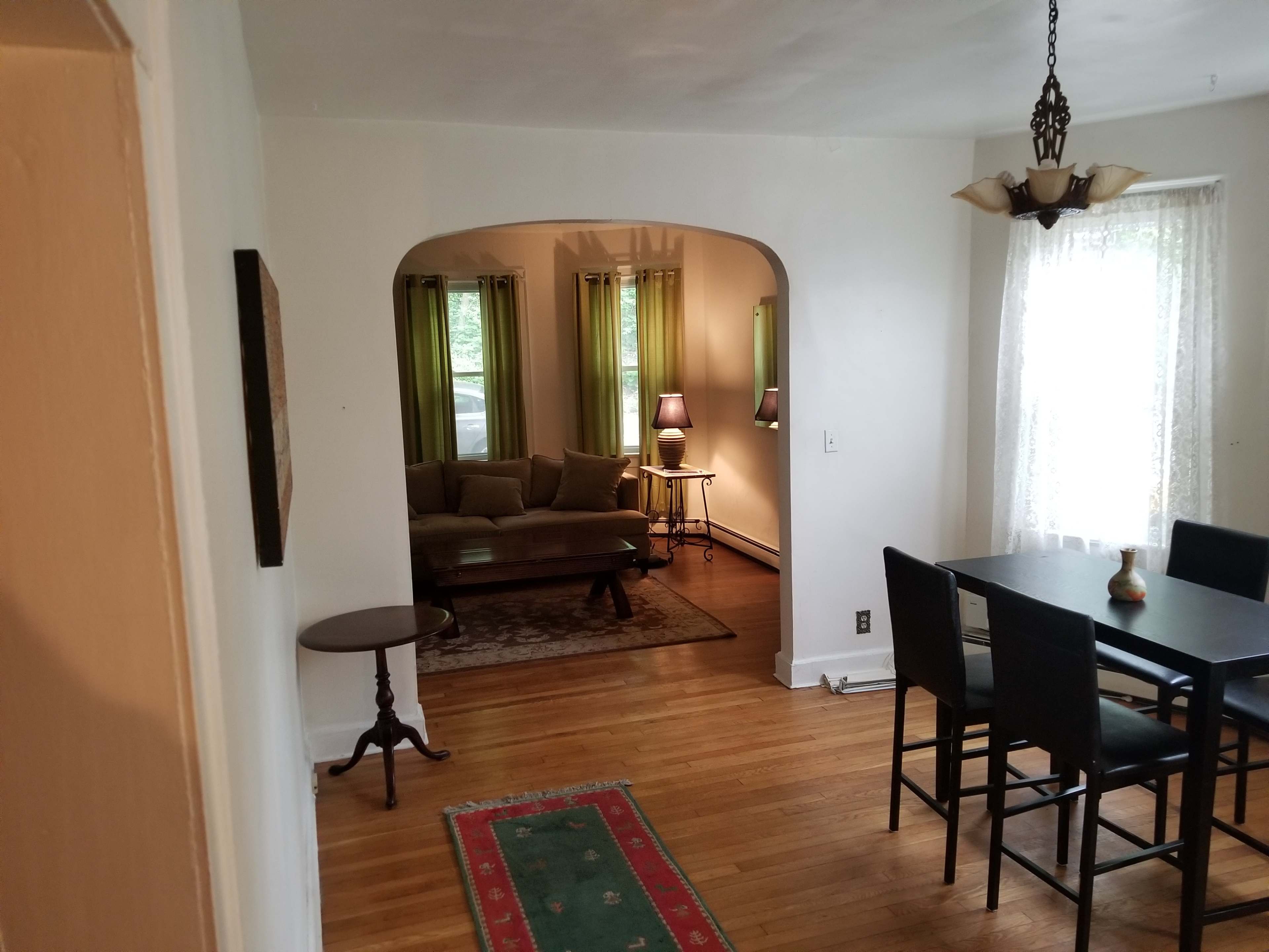 A dining area leading to a living room, with a table, chairs, and a rug visible in the foreground.