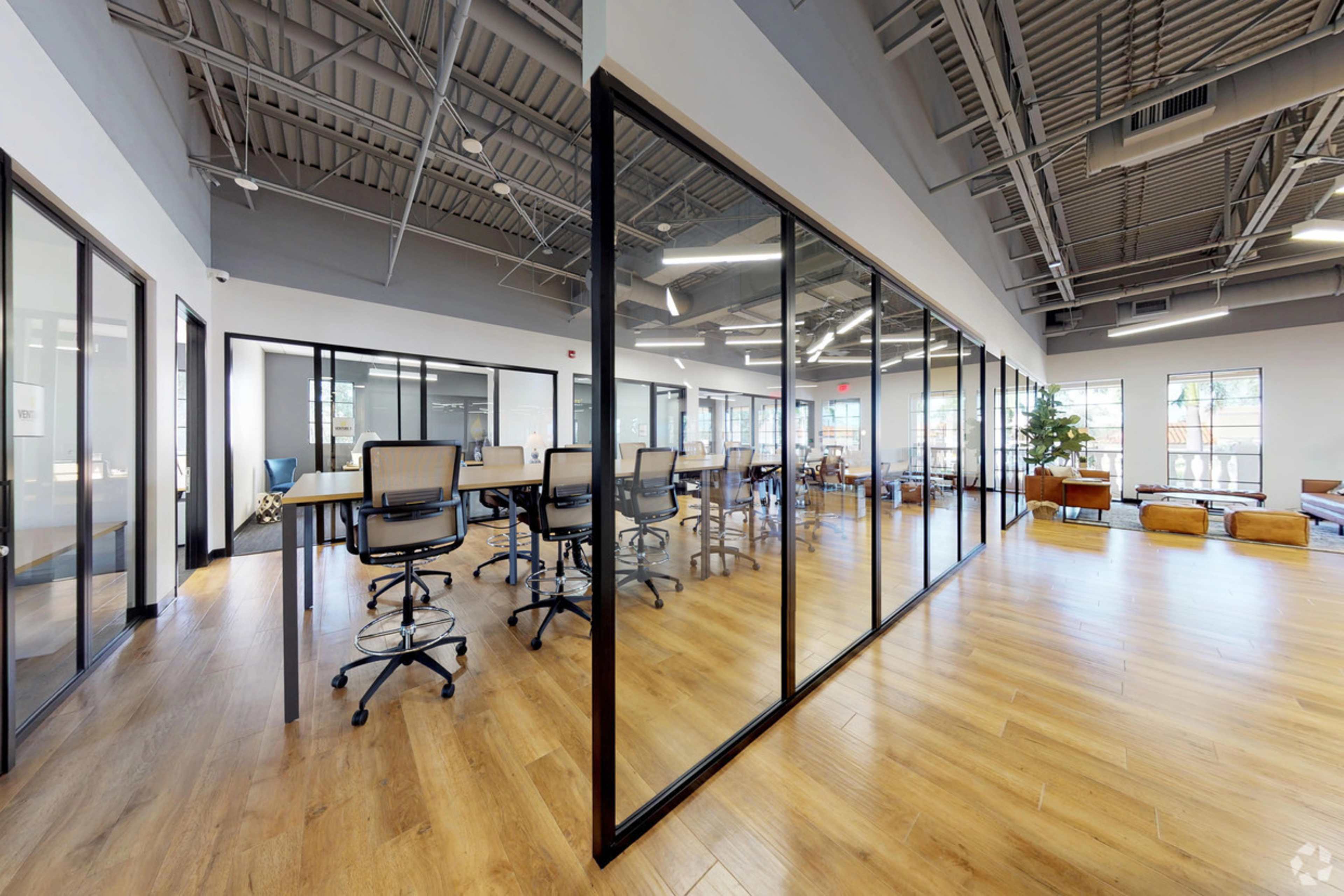 A modern office space with glass-walled meeting rooms, wooden flooring, and a bright, open layout.