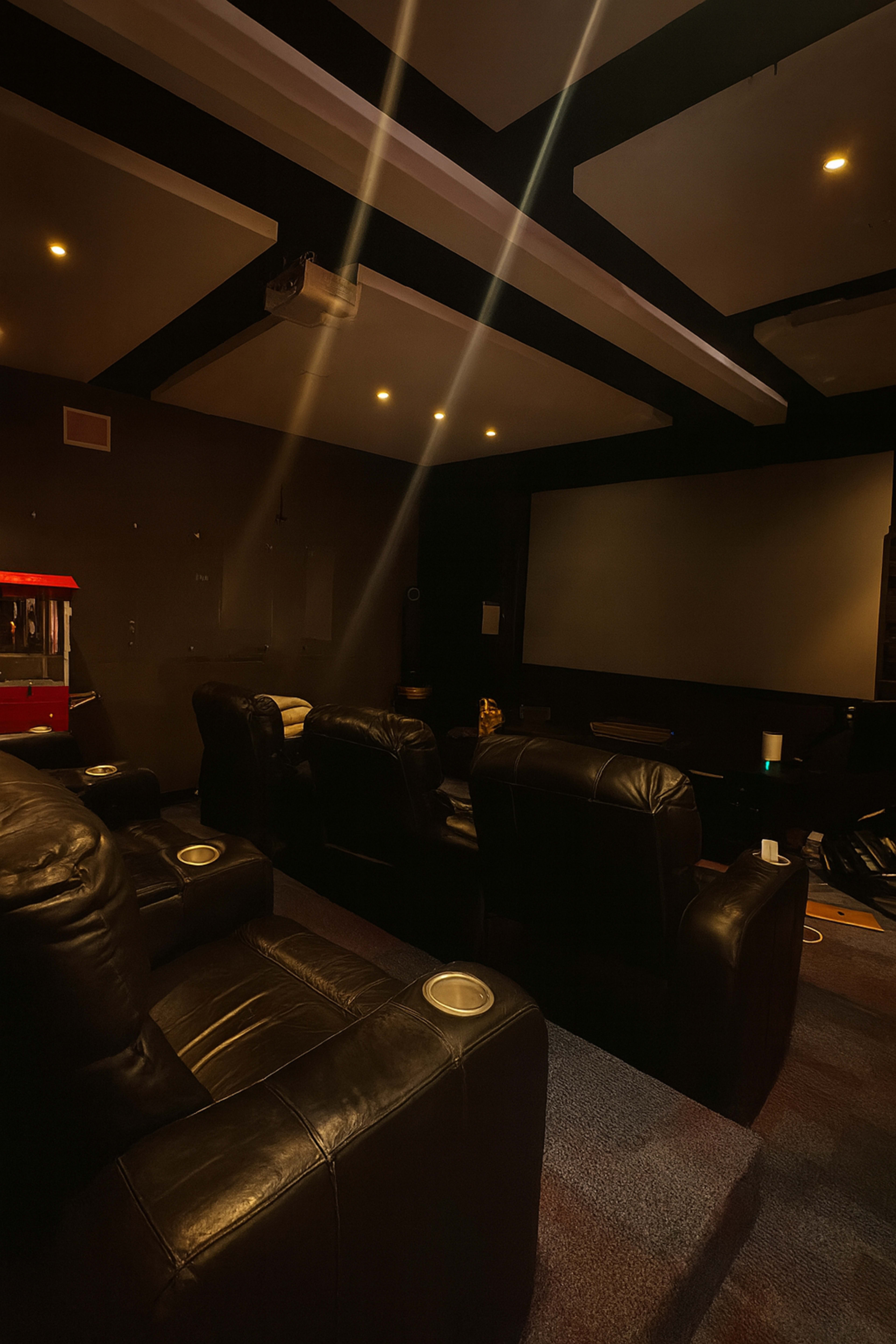 The image shows a dimly lit home theater room with black leather seating and a large screen at the front.