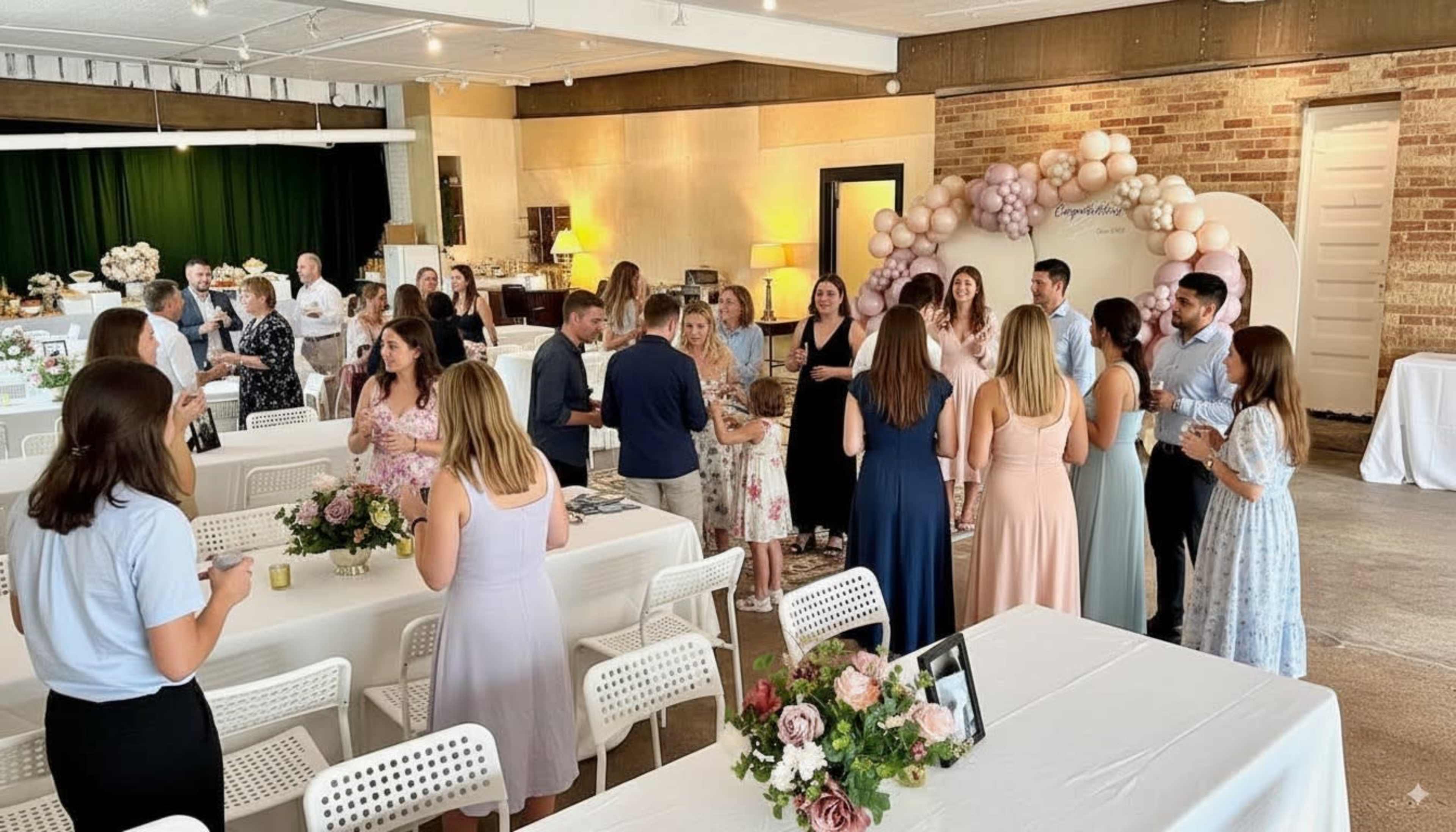 A group of people gather in a well-decorated event space with tables and a balloon arch in the background.