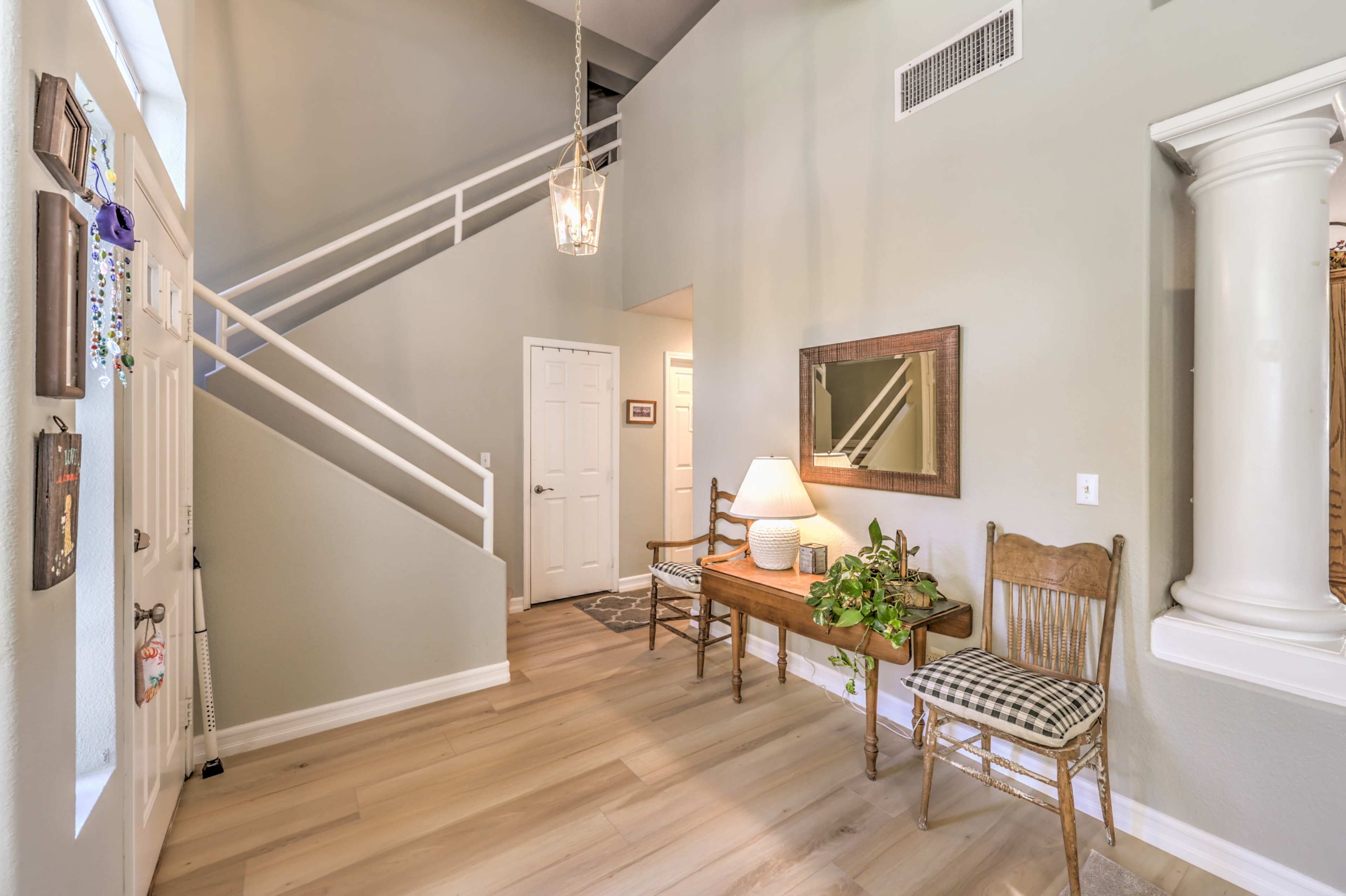 A well-lit entryway featuring a staircase, a small table with a lamp and a plant, and two wooden chairs against the wall.