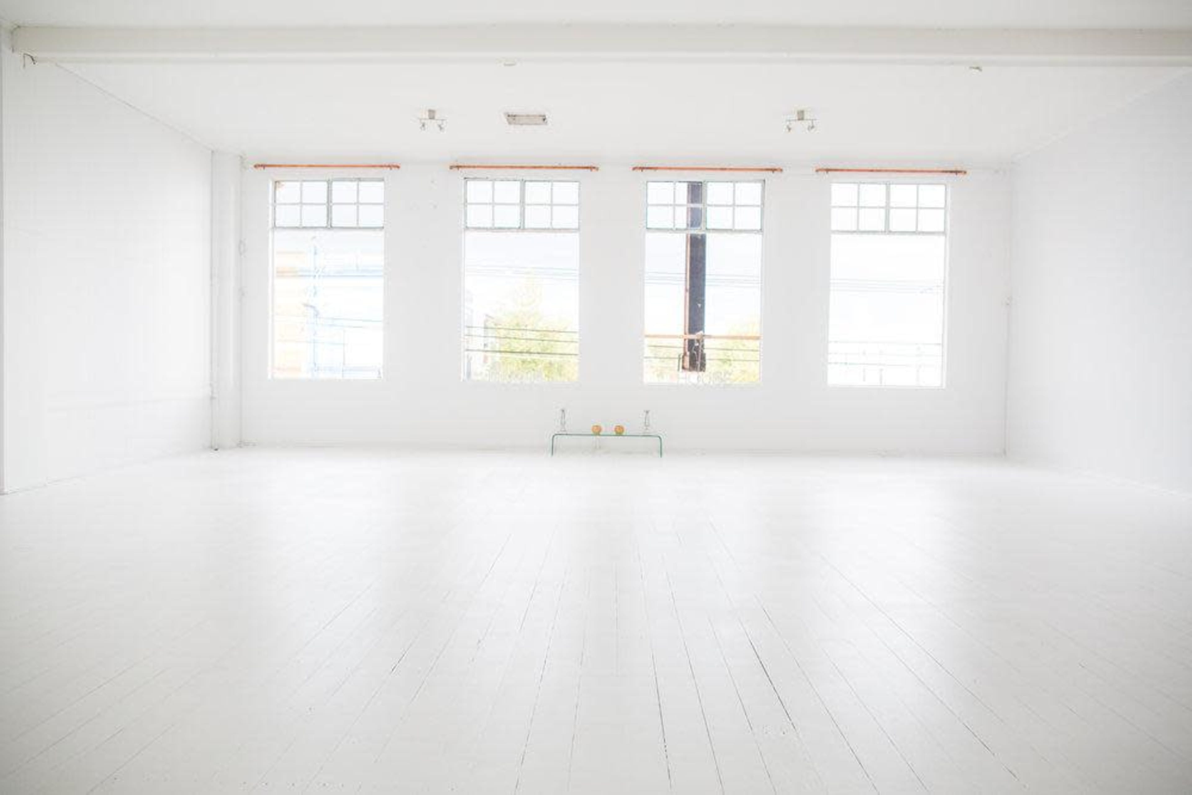 The image shows a spacious, brightly lit room with white walls and large windows allowing natural light to enter.