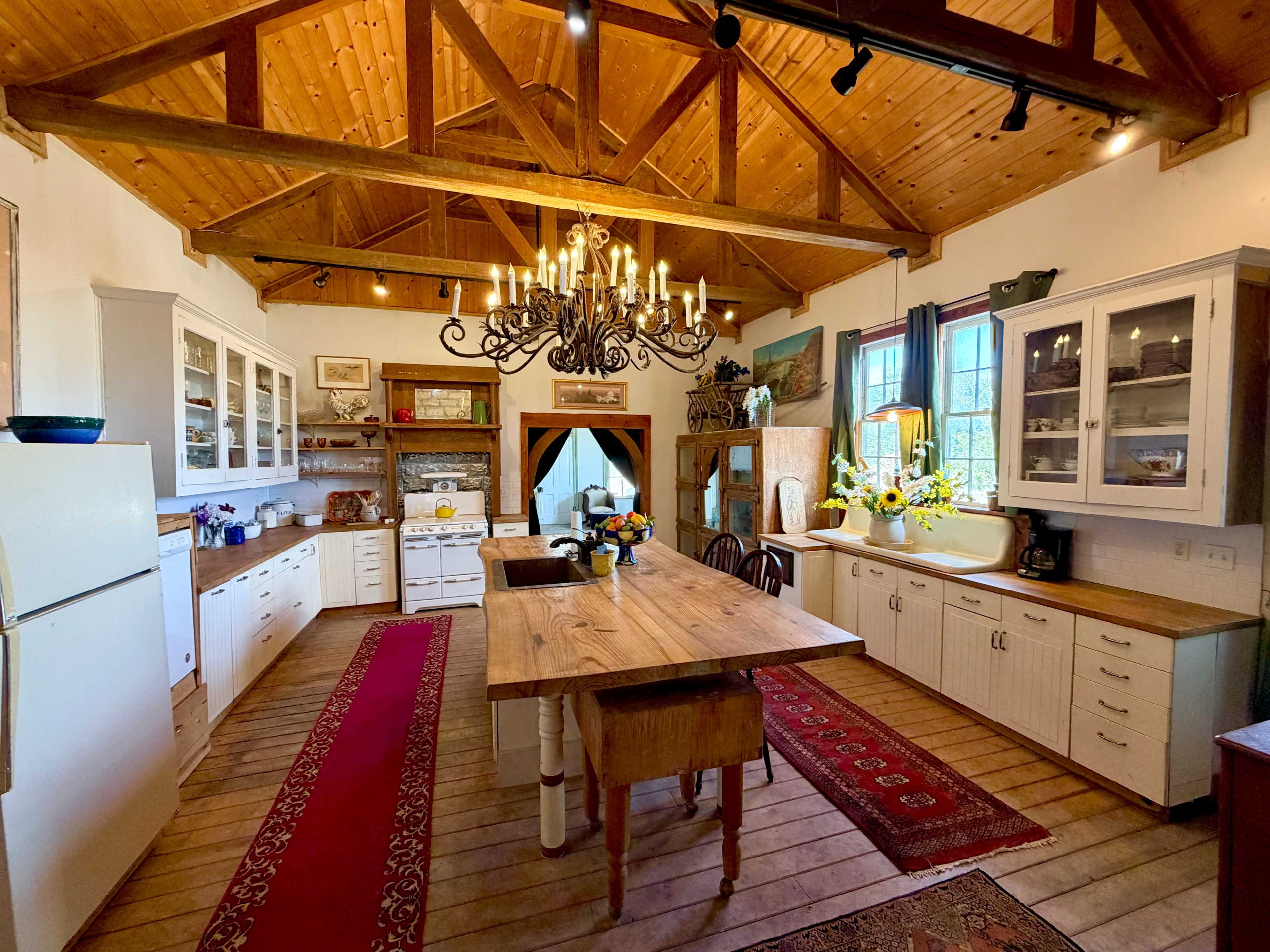 The image depicts a spacious kitchen with wooden ceilings, a large island in the center, and an arrangement of cabinets and appliances along the walls.