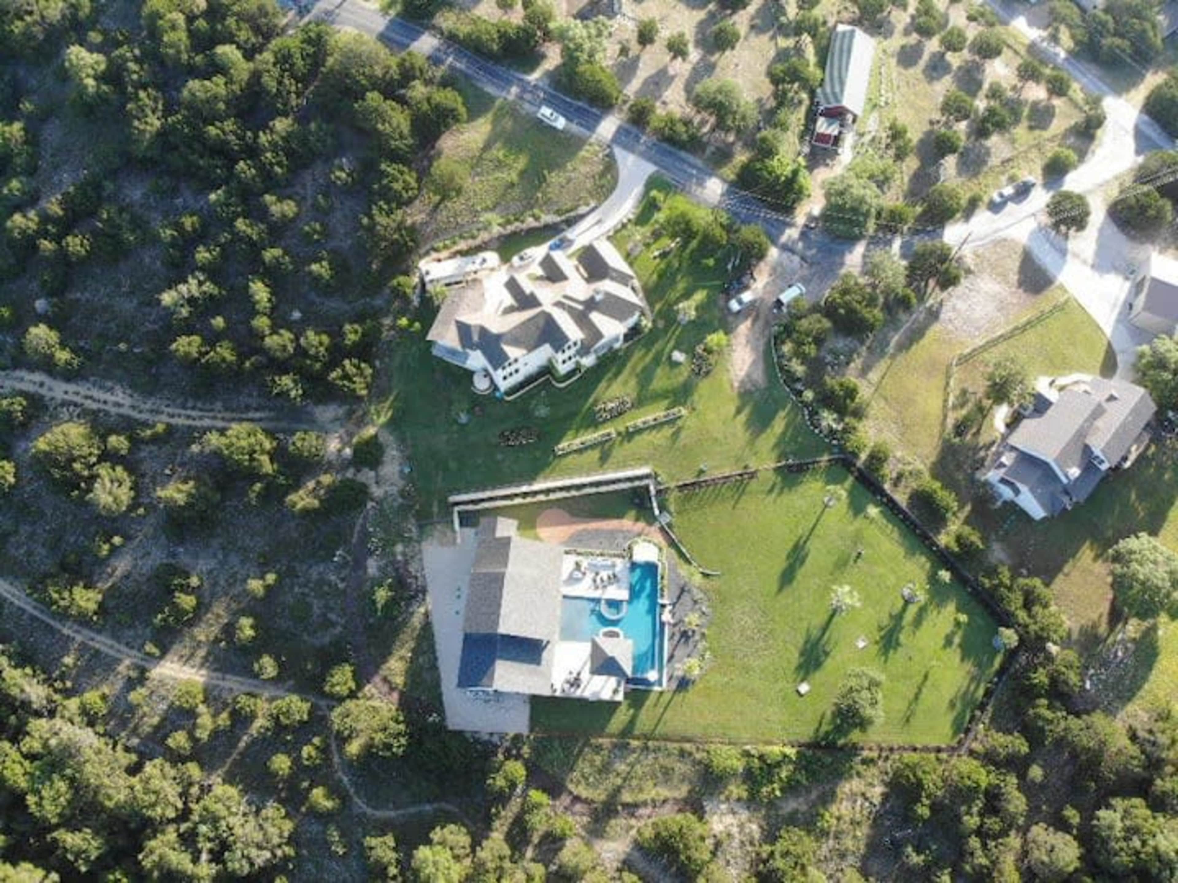 The image shows an aerial view of multiple houses situated in a green landscape with a pool and surrounding trees.
