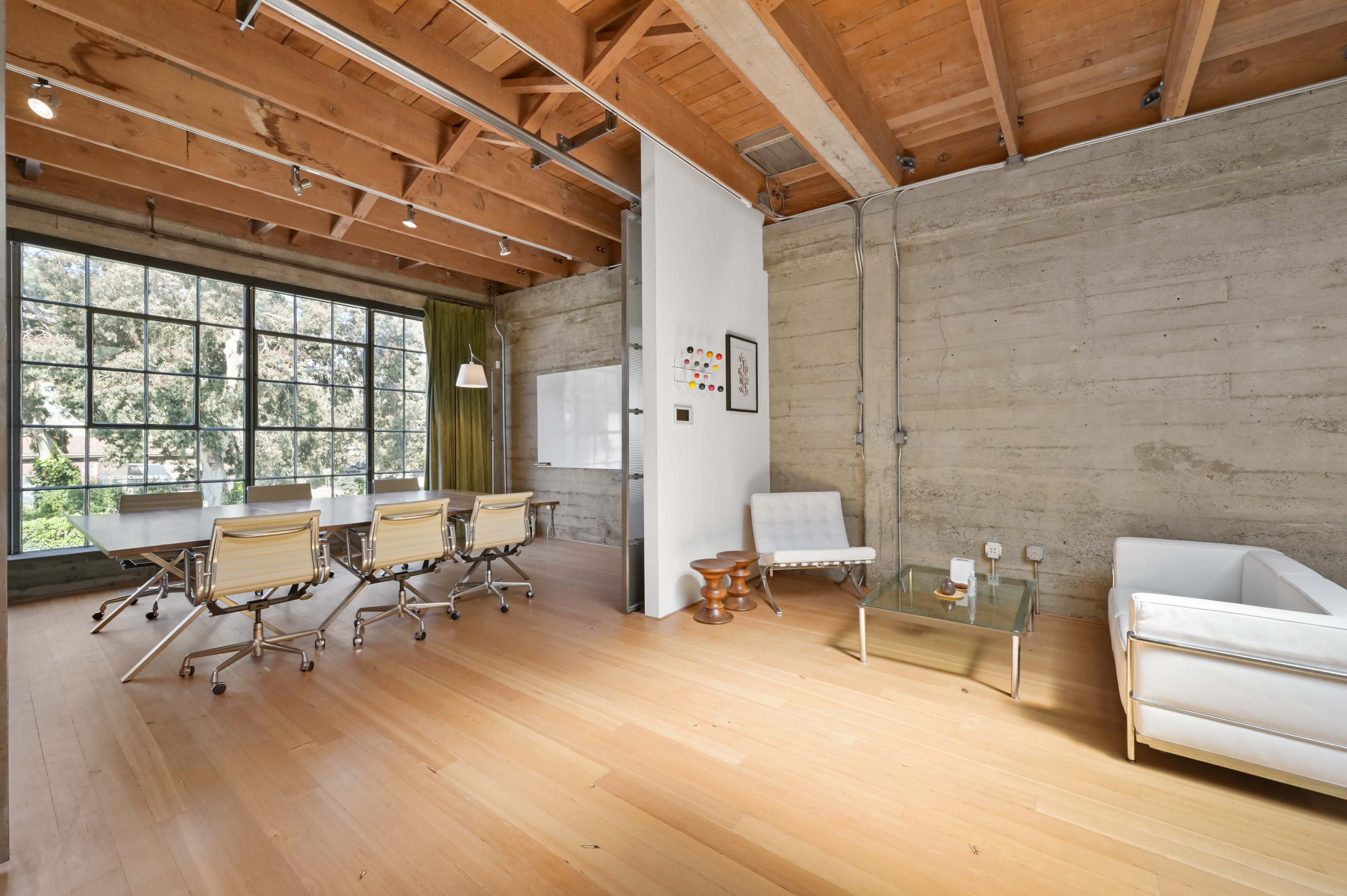 A modern office space with large windows, wooden beams, and a minimalist design featuring a glass coffee table and white furniture.