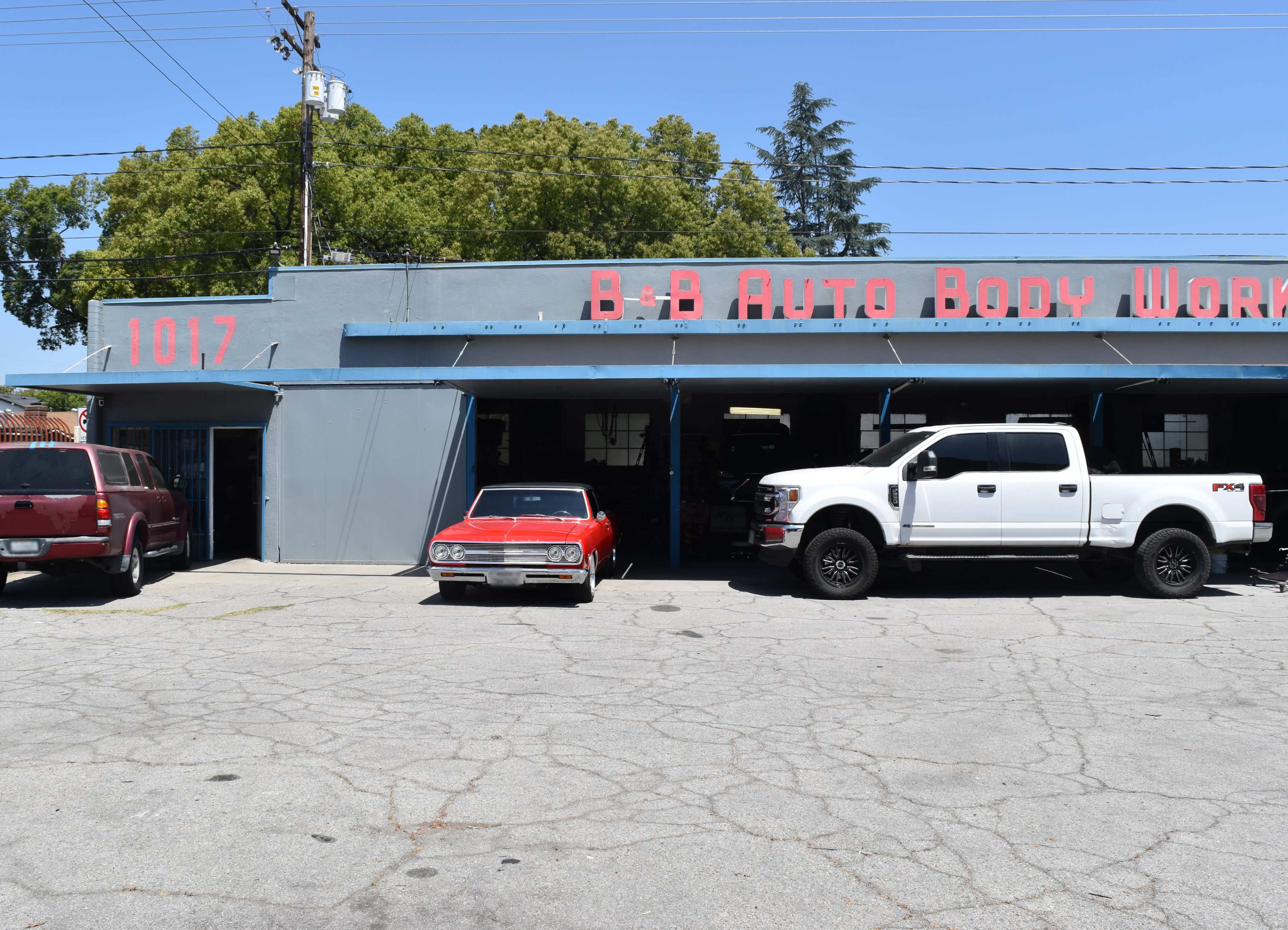 The image shows a garage named "B & B Auto Body Works," featuring a classic red car and a white pickup truck parked in front on a sunny day.