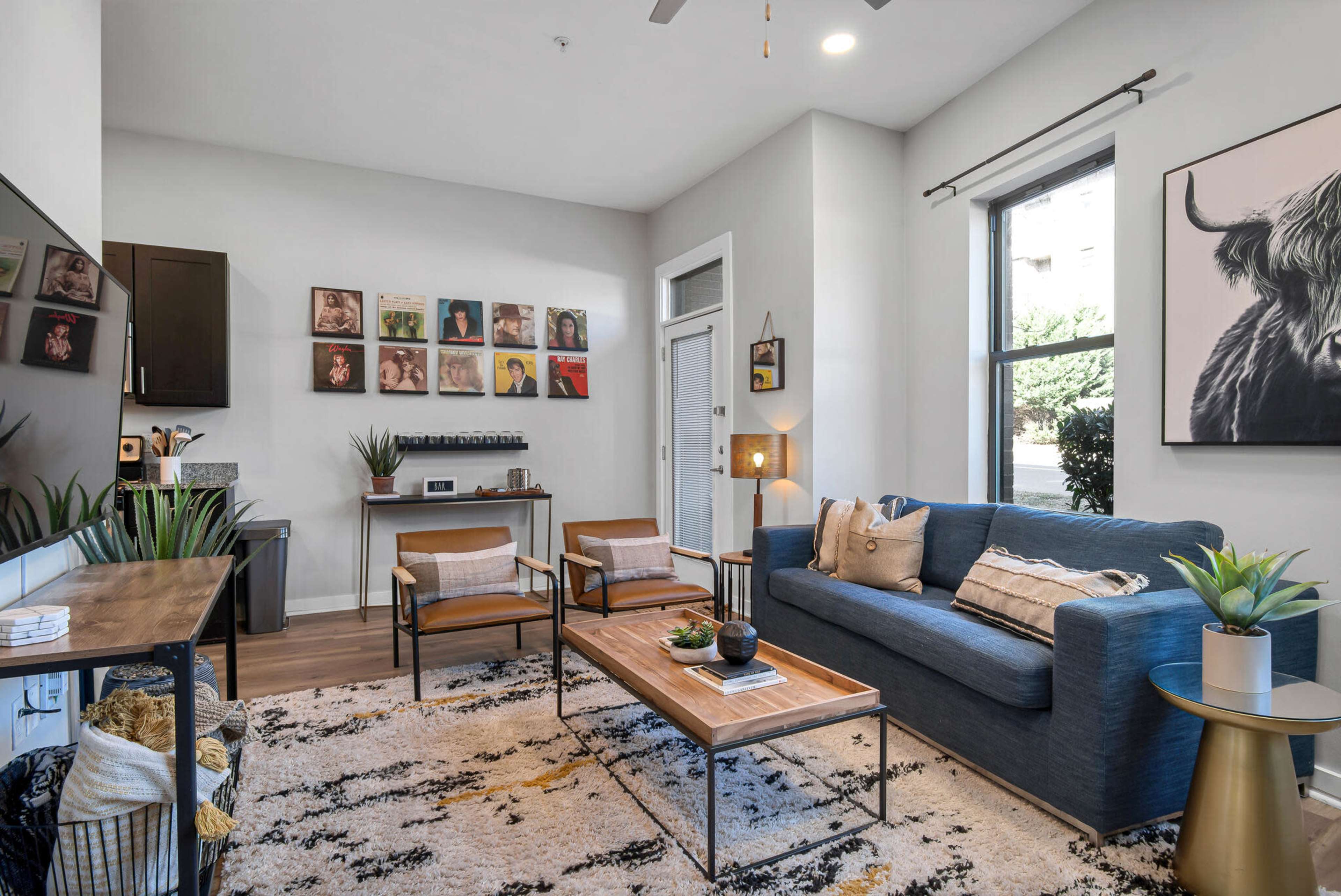 A cozy living room features a blue sofa, two armchairs, a wooden coffee table, and a wall adorned with framed artwork.