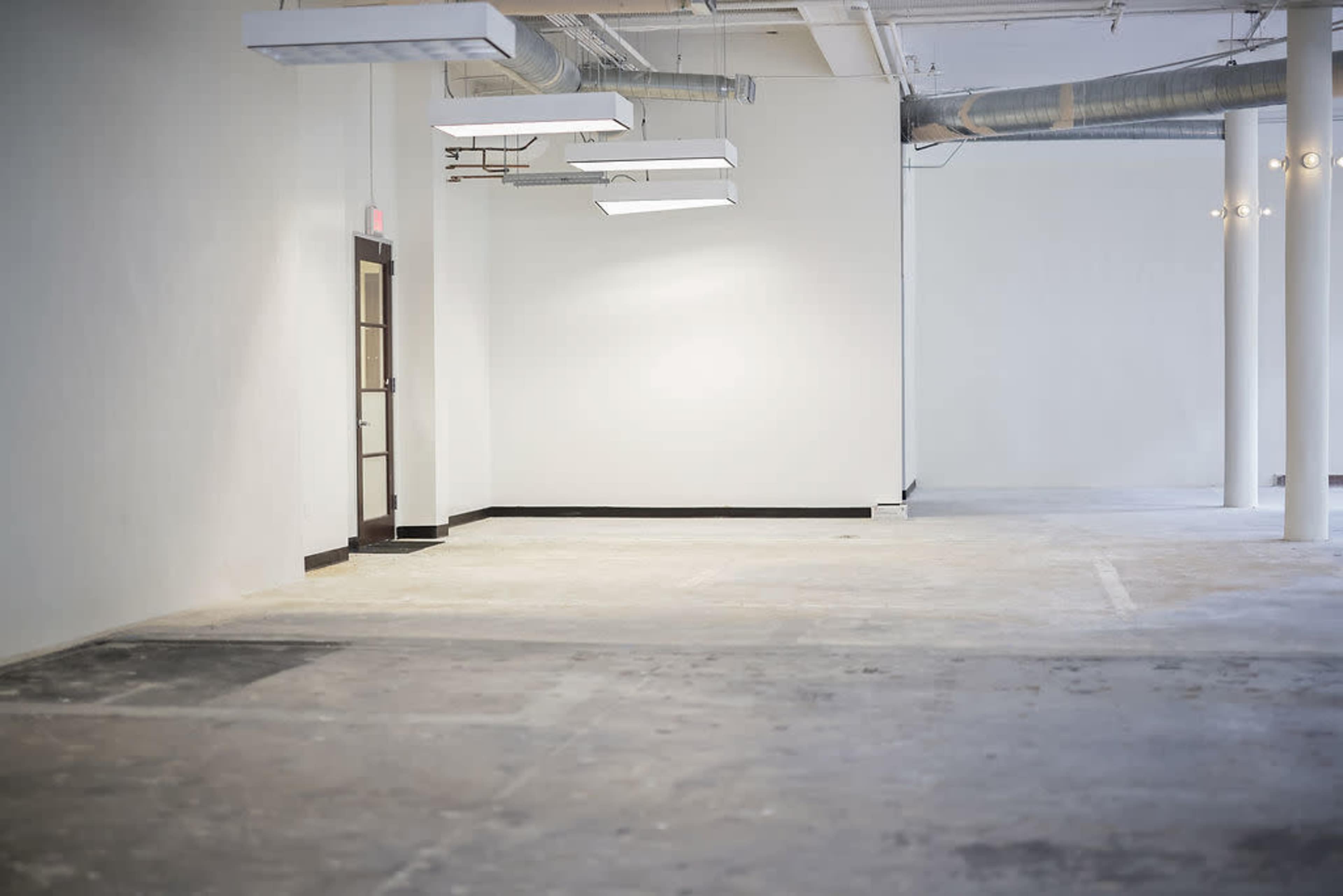 An empty industrial space with concrete flooring, white walls, and exposed ventilation ducts.
