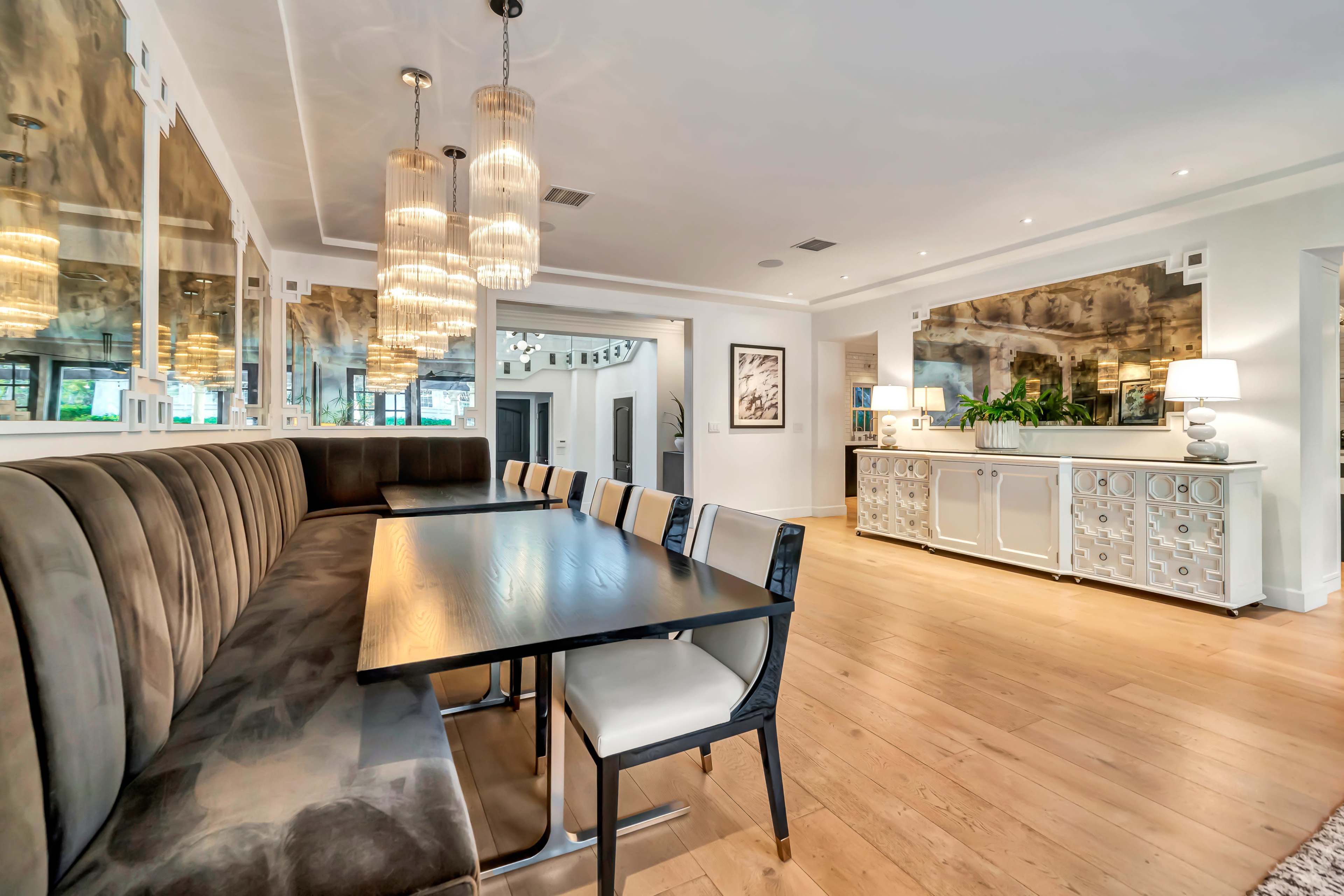 The image shows a modern dining area featuring a long black table with a mix of black and white chairs, a stylish bench, and elegant lighting fixtures.