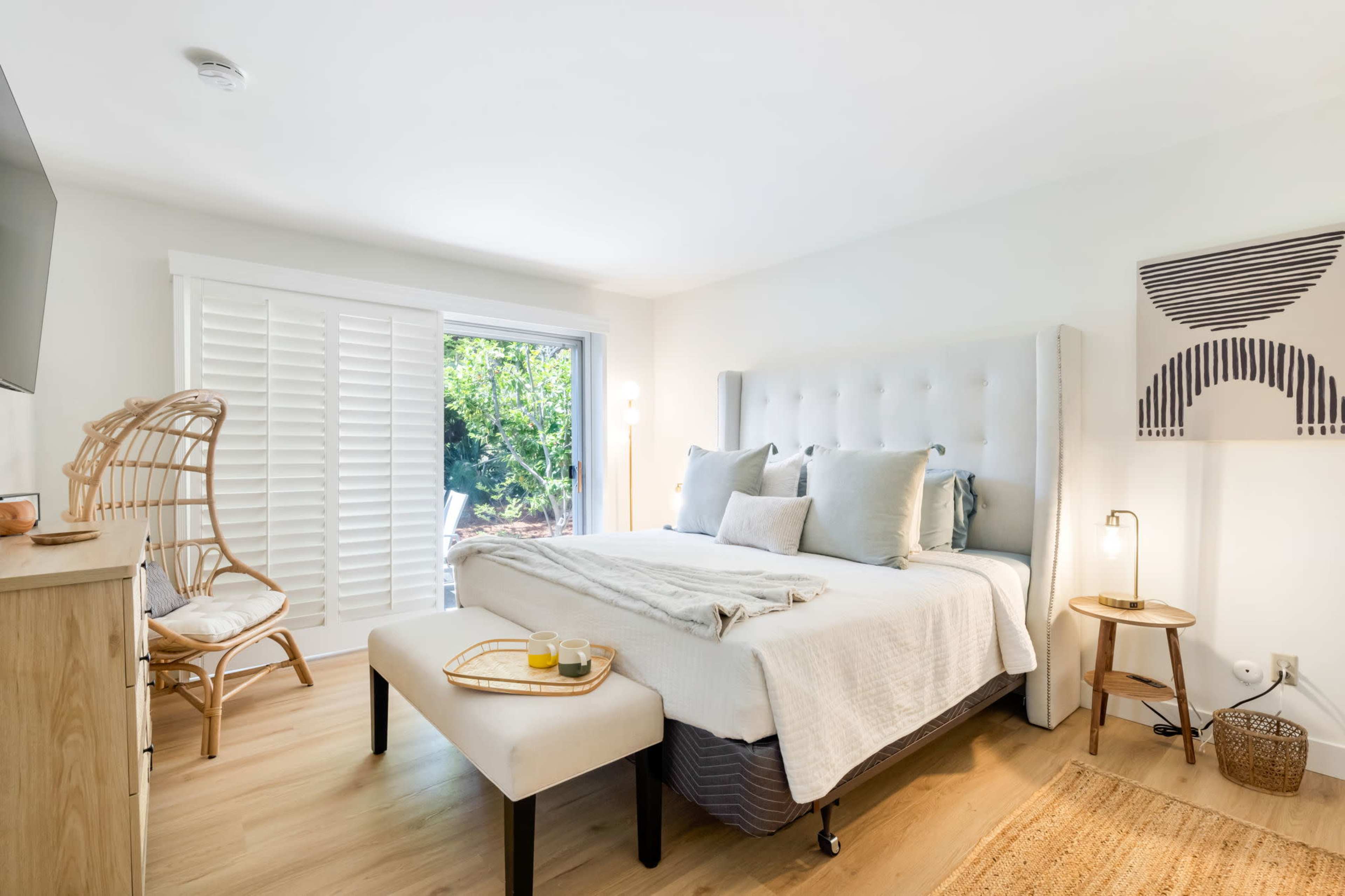 A bright bedroom with a large bed, a wooden chair beside a window, and a bedside table with a lamp.